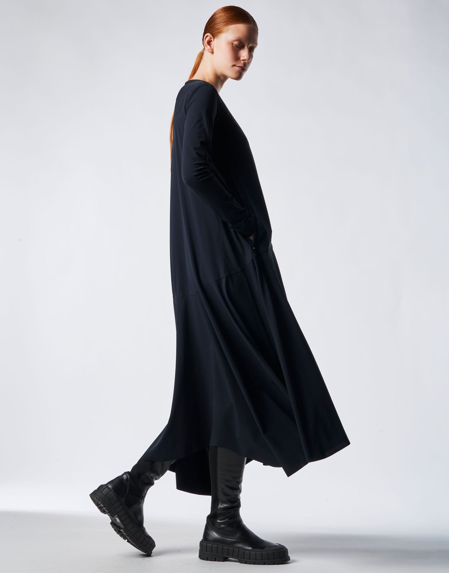 Seitenansicht des MAYBE Kleids in navyblauem Sensitive(R)-Jersey, mit langen Ärmeln, V-Ausschnitt, leicht ausgestellter Silhouette und längerem Saum hinten.