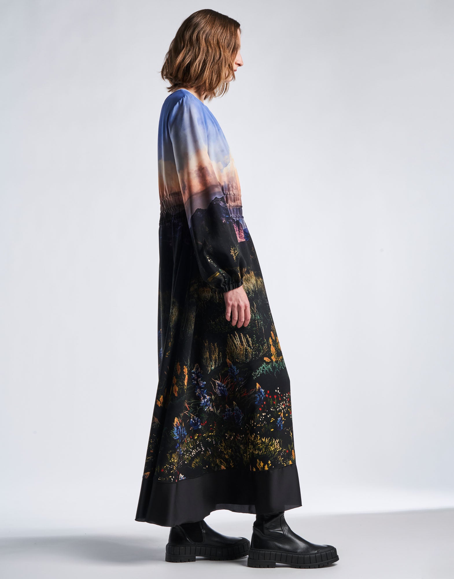Side view of a person wearing the RHYMING maxi-dress in technical crepe with multicoloured Wyoming landscape print, flared skirt and long bell sleeves.
