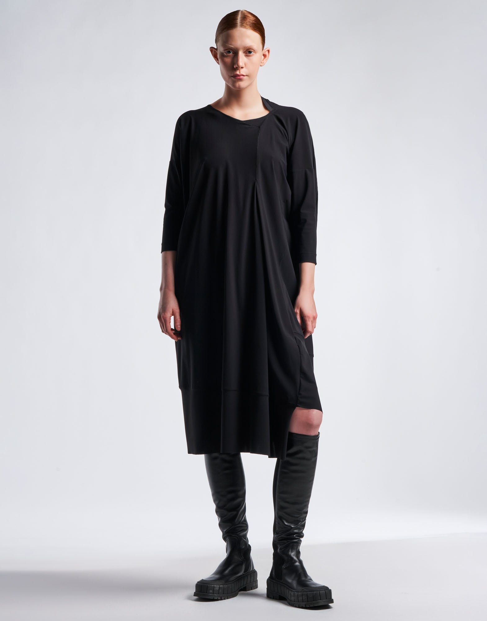 Front view: Model wears PRELUDE dress in black Sensitive(R) jersey with asymmetrical cut, diagonal seams, and three-quarter sleeves.
