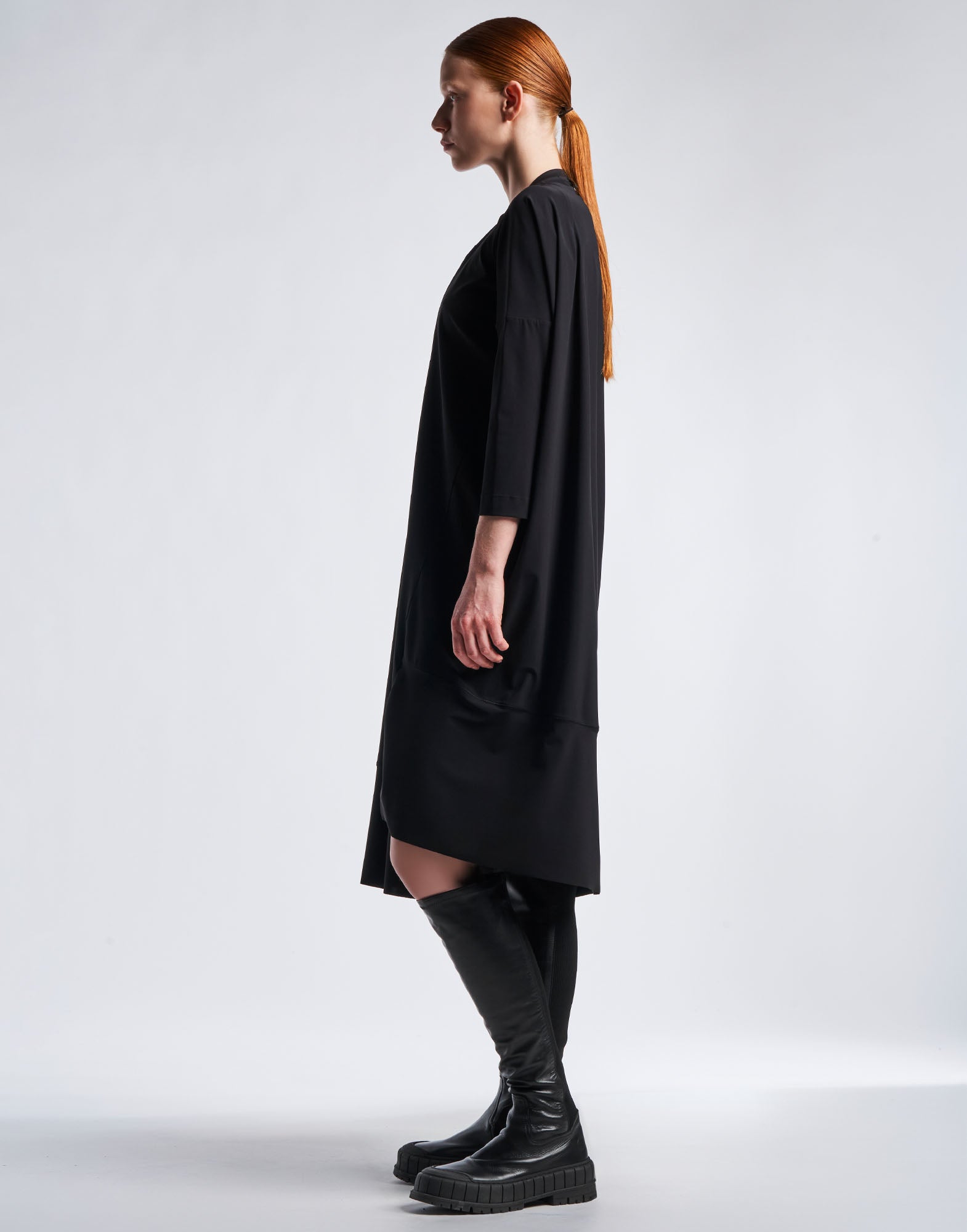 Seitenansicht eines Models im PRELUDE: Ein schwarzes, gerade geschnittenes Kleid aus sportlichem Sensitive(R)-Jersey mit asymmetrischem Saum und Dreiviertelärmeln.