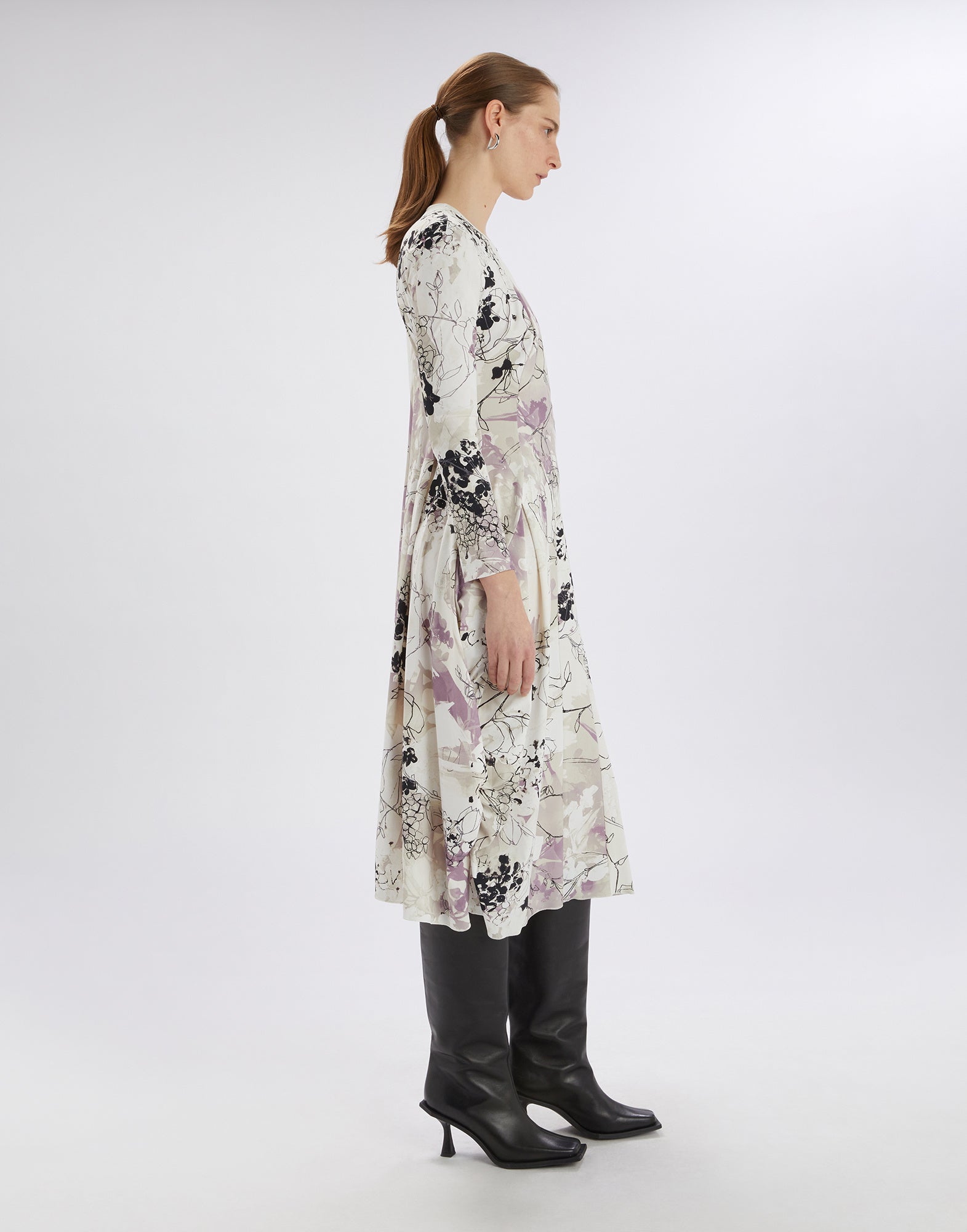 Side view of the AT-LENGTH dress with floral Layered Flowers print, V-neckline, and long balloon shape, worn by a woman with black boots.