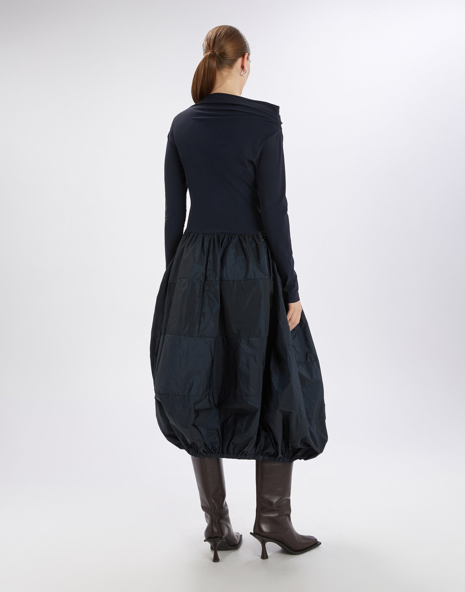 Rear view: Eine Frau trägt das Kleid GRID mit schlichtem Sensitive(R)-Korsett, langen Ärmeln und ballonförmigem Rock aus glänzendem technischem Taft.