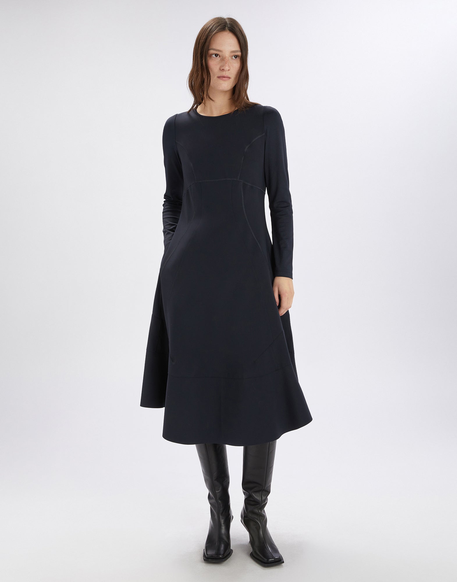 Frontalansicht: Modell trägt das minimalistische, dunkelblaue SYNCHRO Kleid mit langen Ärmeln, rundem Ausschnitt, sichtbaren Nähten und asymmetrischem Saum.