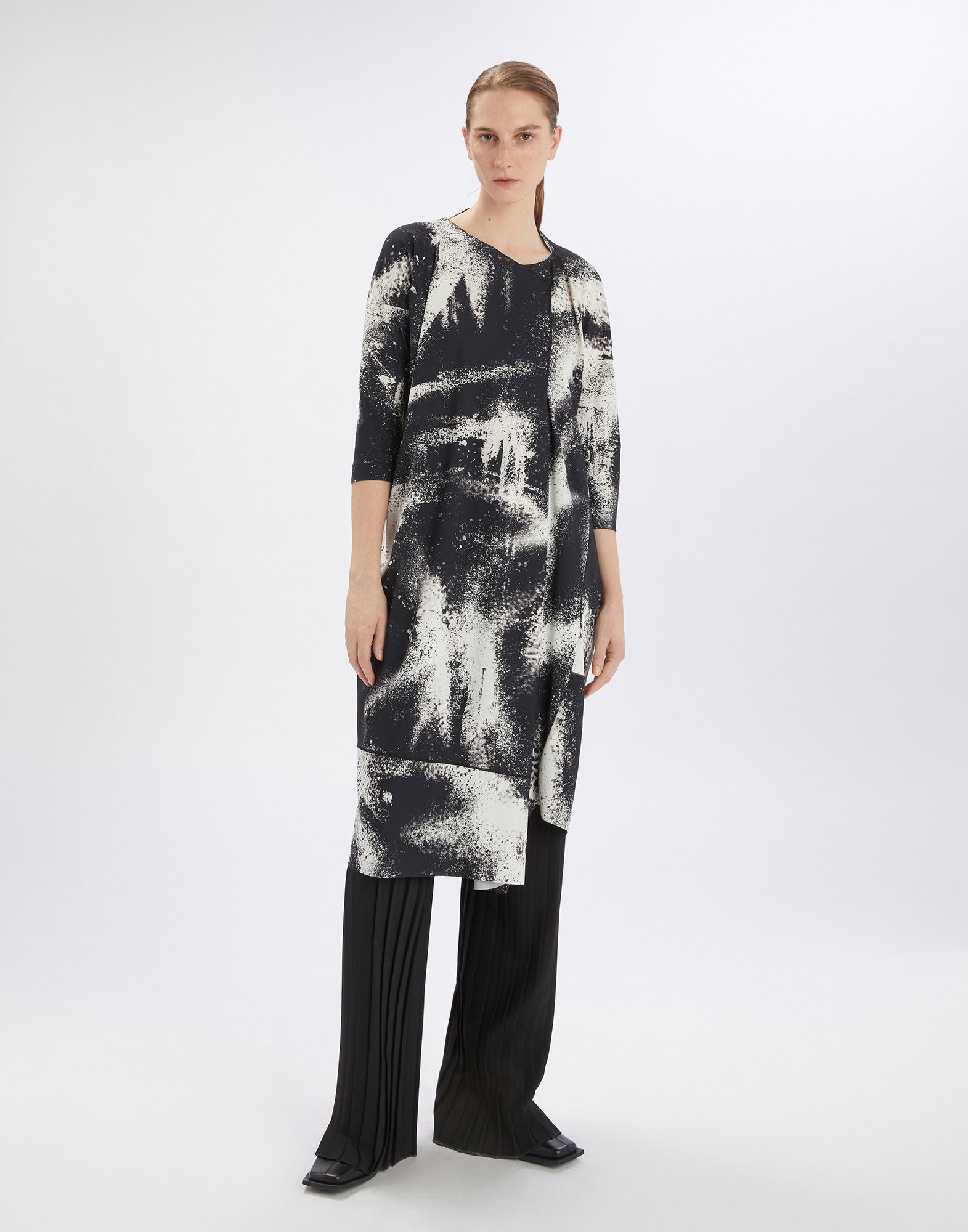Frontalansicht: Modell trägt PRELUDE Kleid mit schwarzem und weißem Spray-Effekt-Druck, dreiviertel Ärmel, asymmetrischem Saum und breiten dekorativen Nähten.