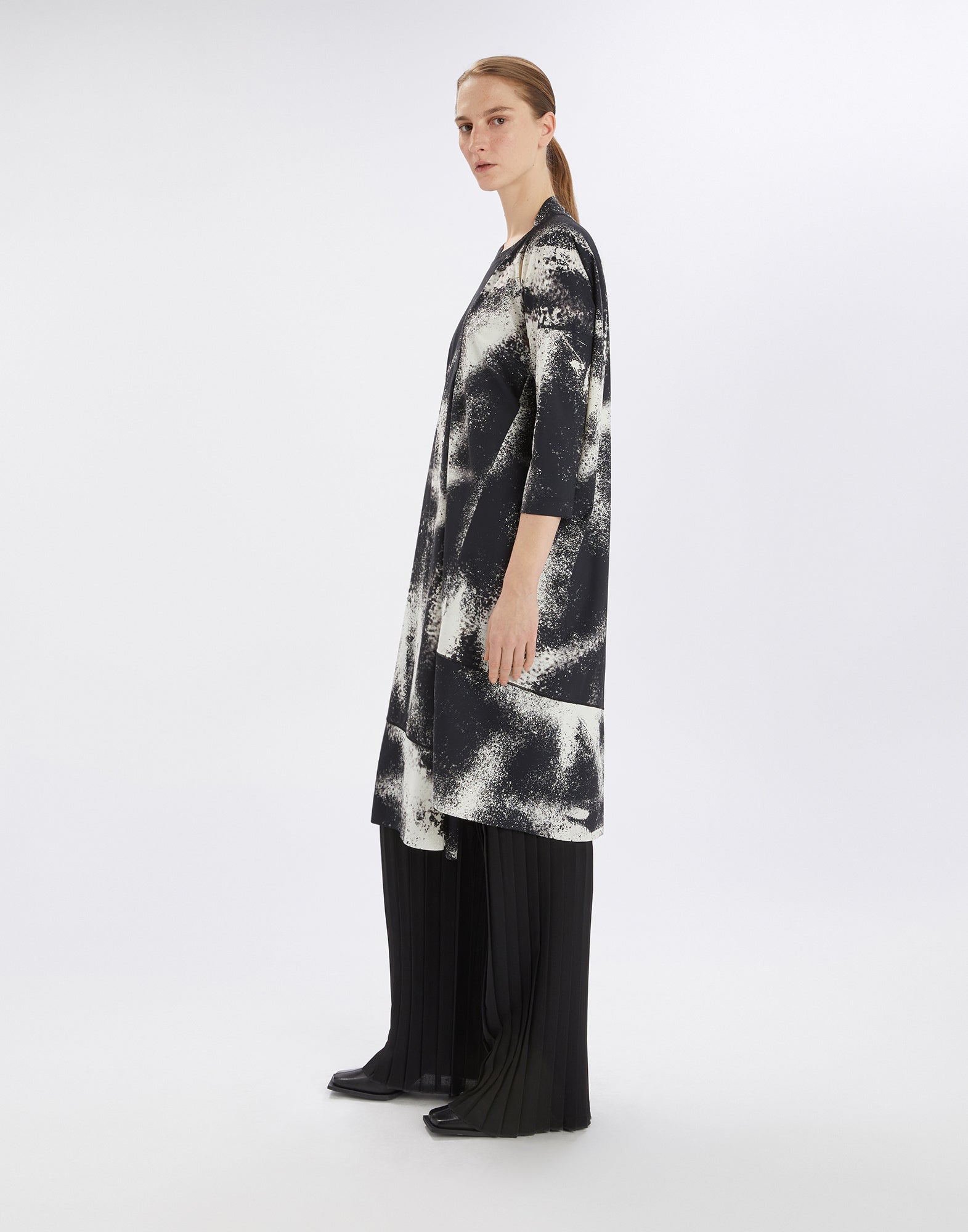 Side view of the PRELUDE dress, black-and-white spray-effect print, asymmetric hem, three-quarter sleeves, worn by a model against a neutral background.