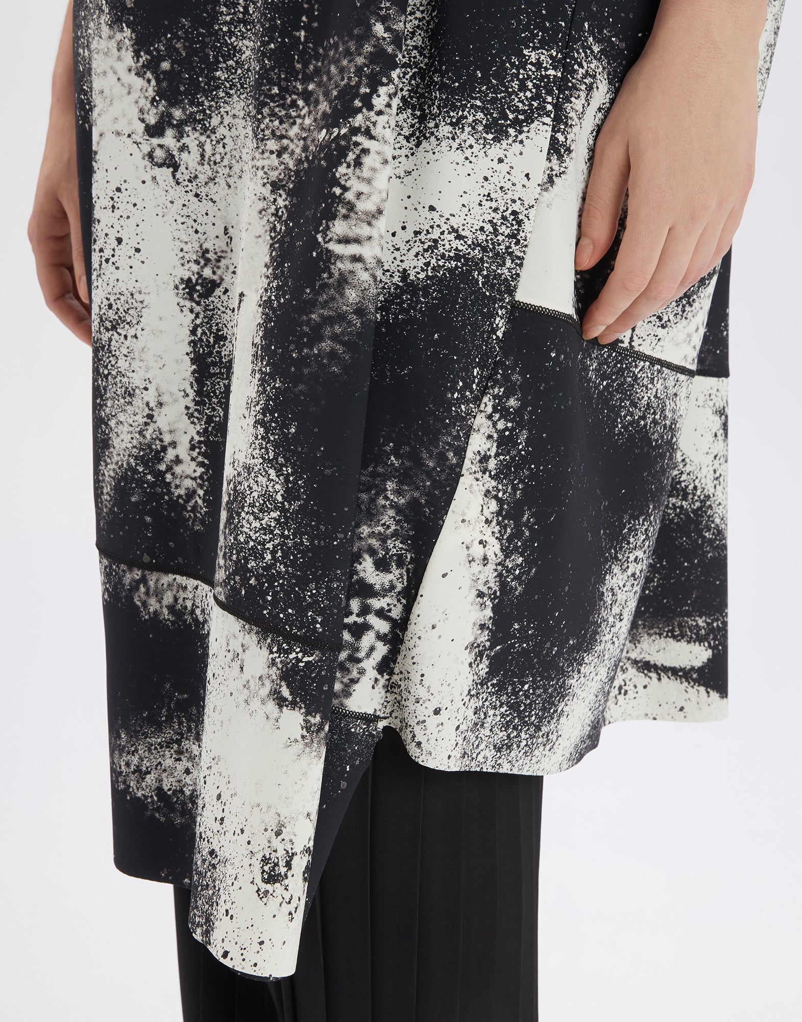Detailed view of the PRELUDE dress with asymmetric hem and black-and-white spray-effect print, focusing on decorative seams at the hem.