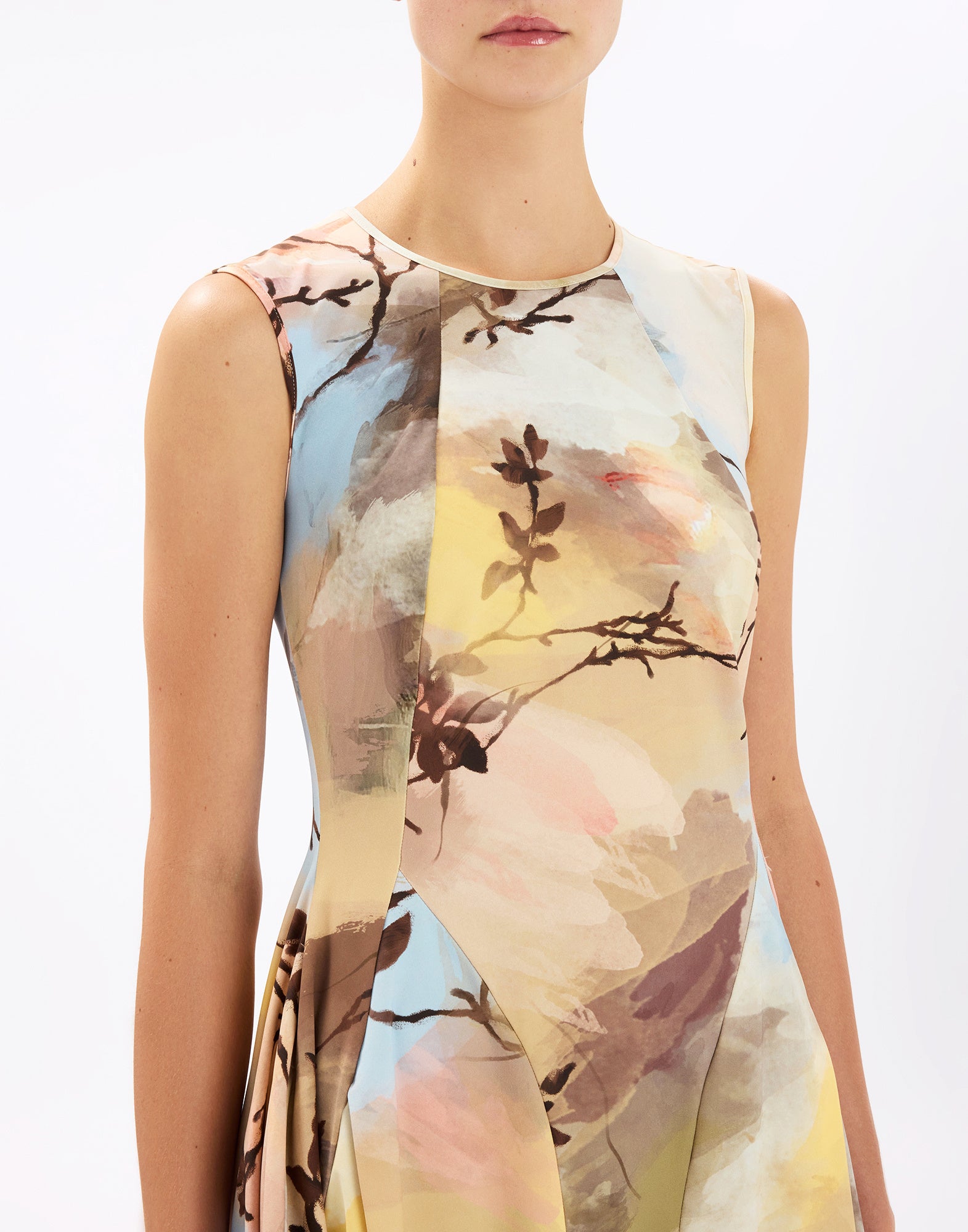 Frontalansicht: Frau trägt ärmelloses AT-LENGTH Kleid mit Rundhalsausschnitt, fließendem Sitz und abstraktem, aquarellartigen Blumen- und Ast-Print in sanften Pastellfarben auf hellem Grund.