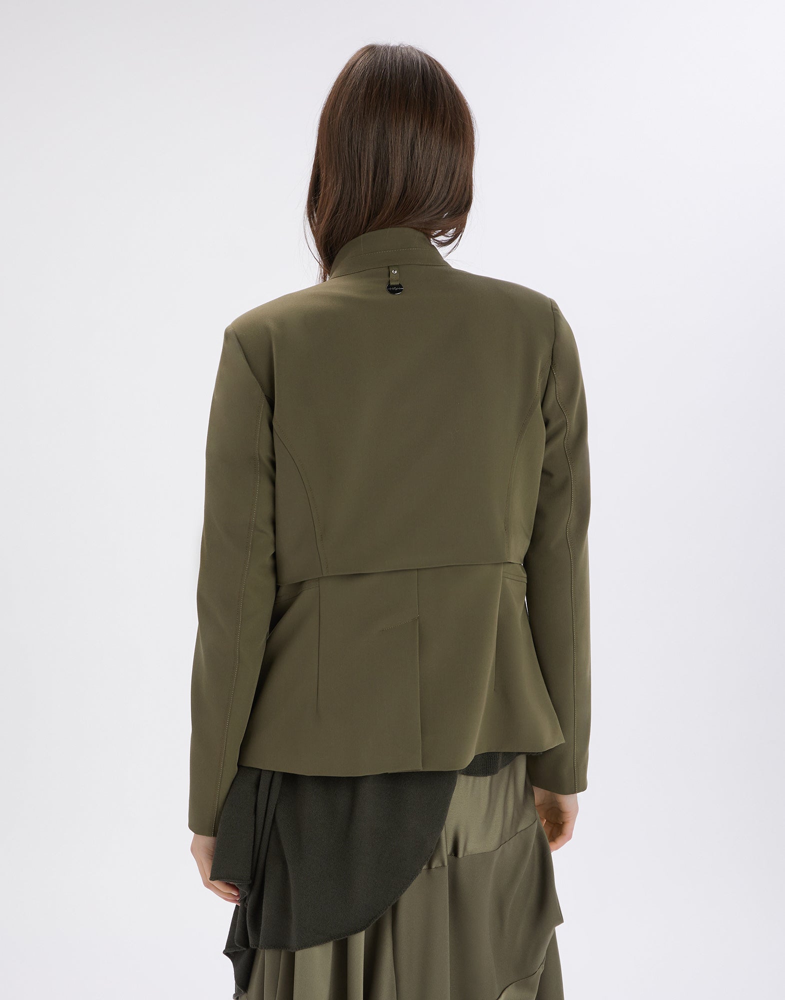 Back view of PARALLAX jacket in olive green technical twill, medium weight, with exposed seams and padded shoulders, worn by a woman.
