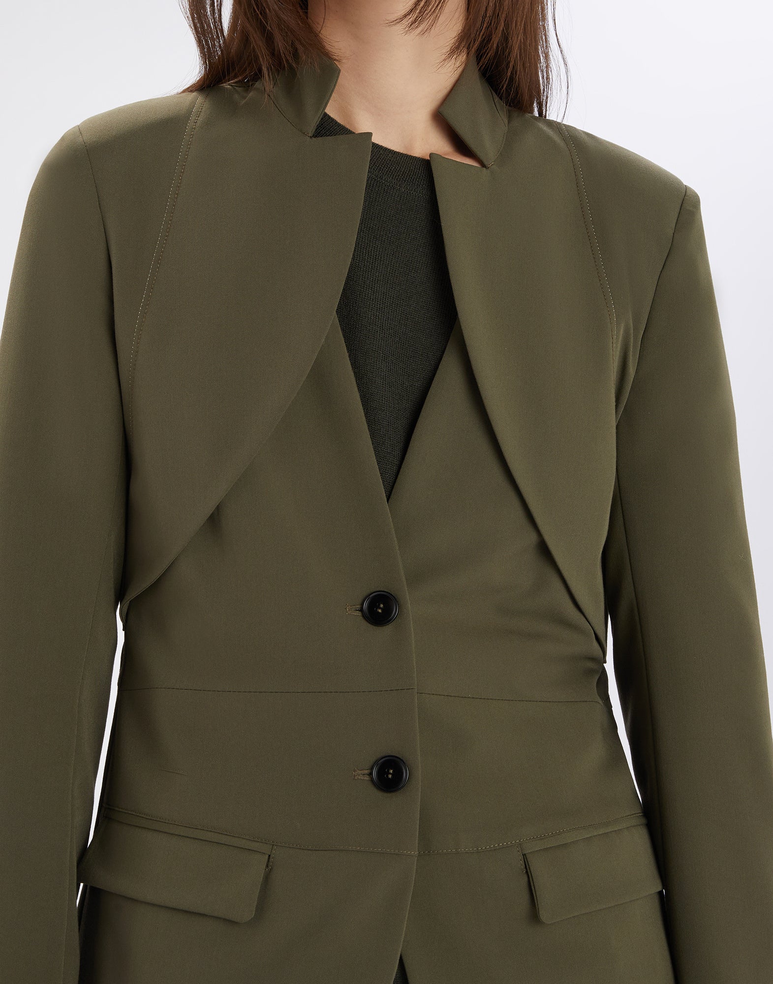 Front view of the PARALLAX jacket, olive technical twill, featuring inverted notched collar, two buttons, geometric neckline, and welt pockets.