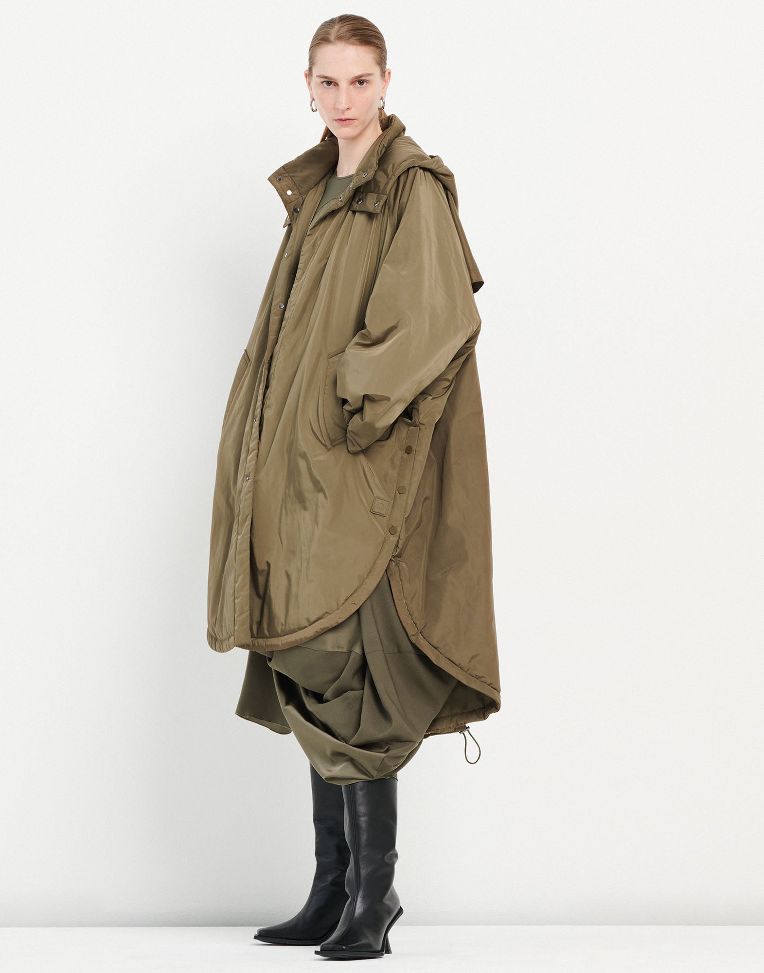 Front view of a person wearing the COFFER parka in olive green. The parka has an oversized fit, wide kimono sleeves, side buttons, hood, and adjustable hem.