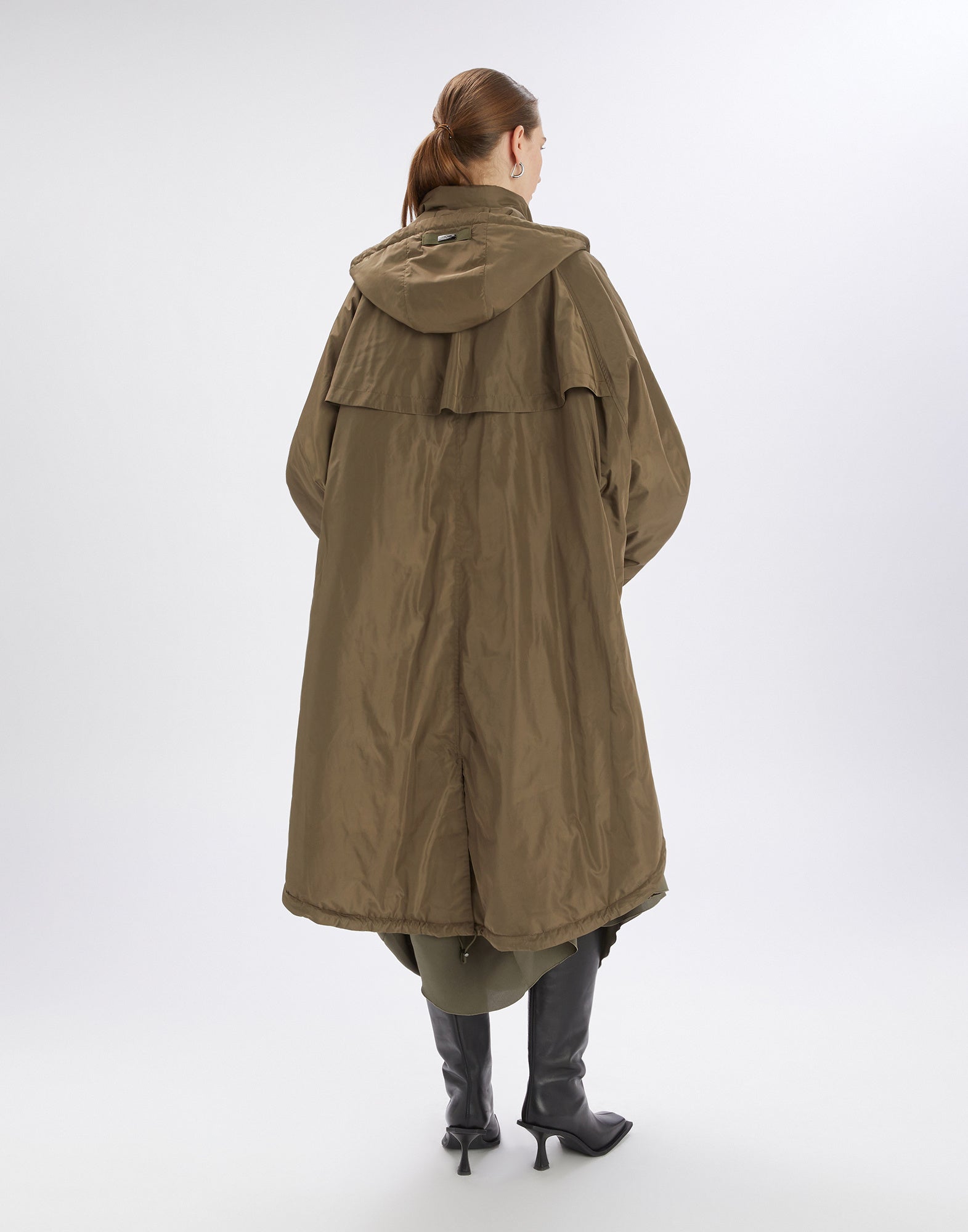 Rückansicht des Parka COFFER in olivgrün mit Kapuze, weitem Oversize-Schnitt und Kimono-Ärmeln, getragen von einer Frau mit Stiefeln.