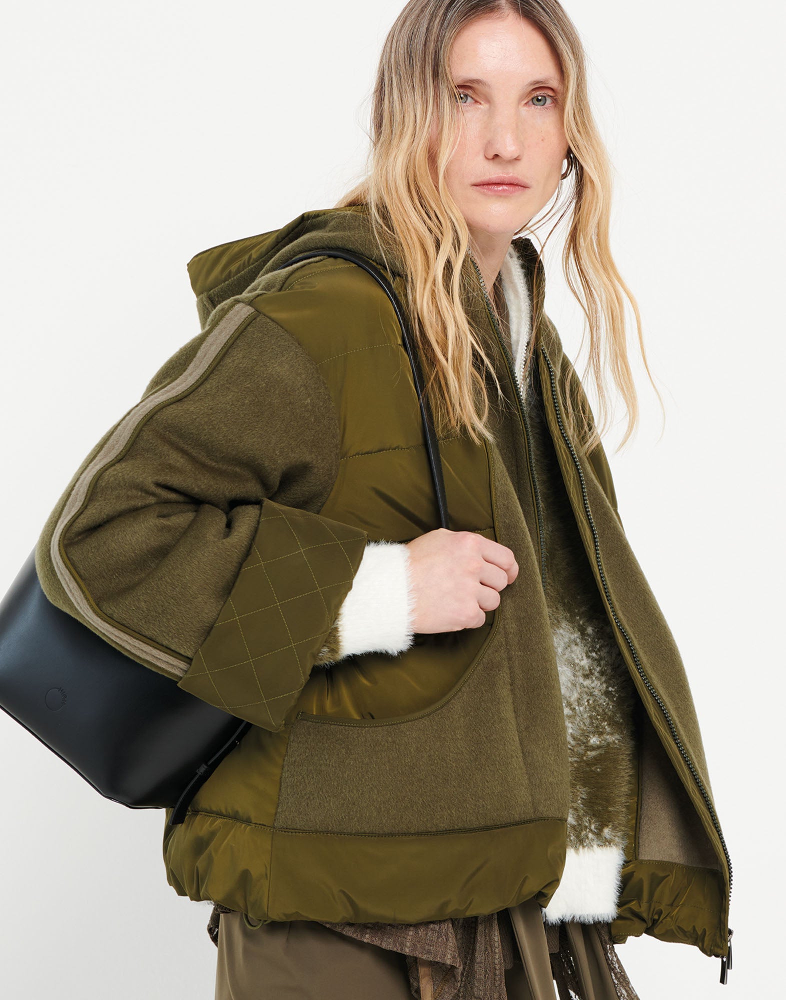 Front view: Person wears the PRIMULA bomber with hood in olive green, padded, with wide kimono sleeves, boxy fit, and side pockets.