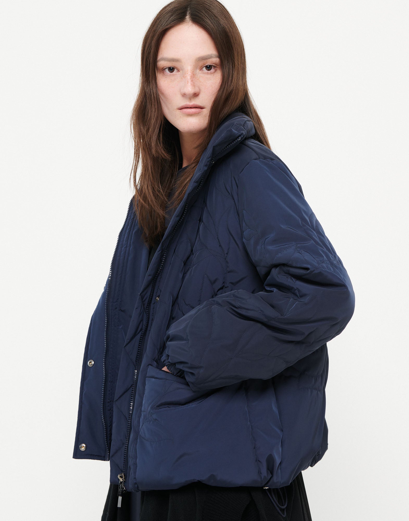 Side view of the BLURT jacket in dark blue, worn by a woman, featuring stand collar, zipper, front patch pockets, and padded floral embroidery.
