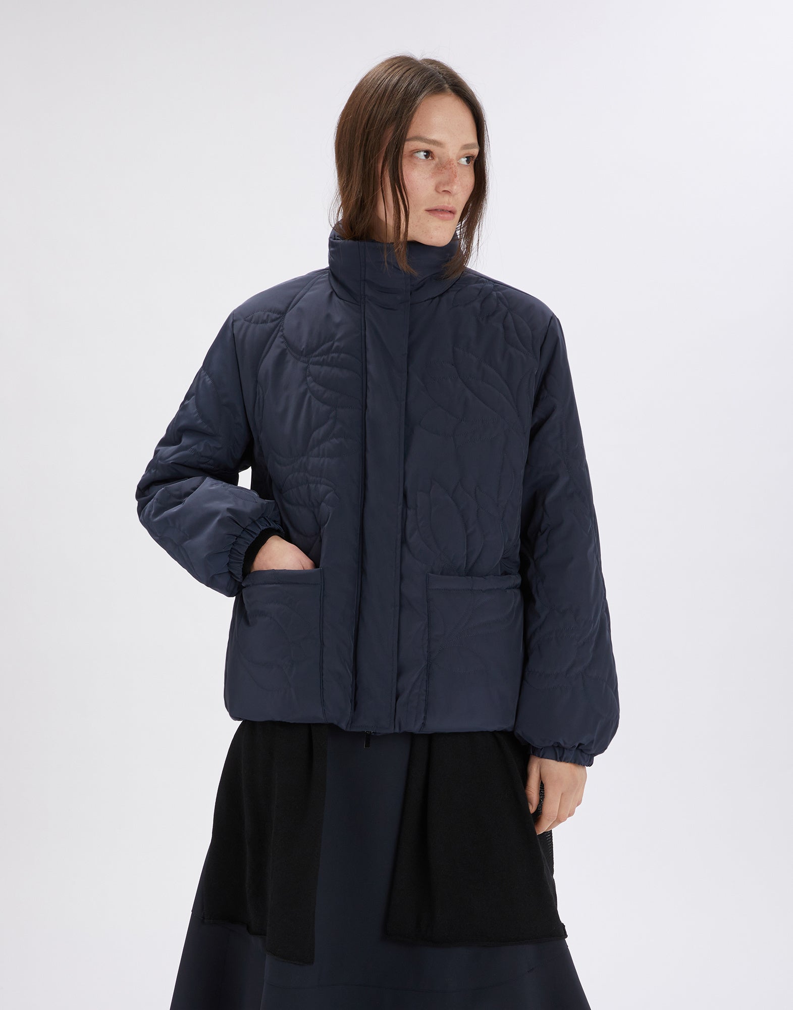 Frontalansicht: BLURT Jacke in dunklem Blau, mittellang geschnitten, mit Stehkragen, gesteppten Blumenmustern, aufgesetzten Taschen und elastischen Bündchen.