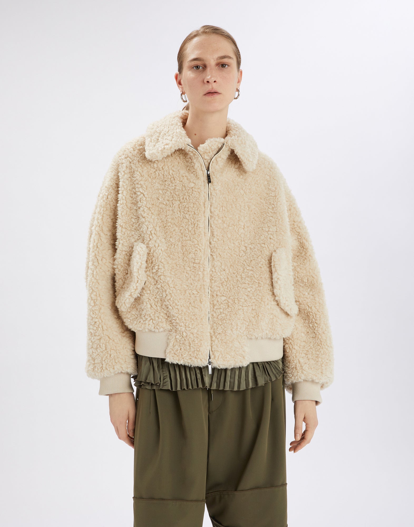 Front view: Person wears the RULER Sherpa bomber jacket in creamy bouclé faux fur with turned-down collar, side flap pockets, zipper, and ribbed cuffs.