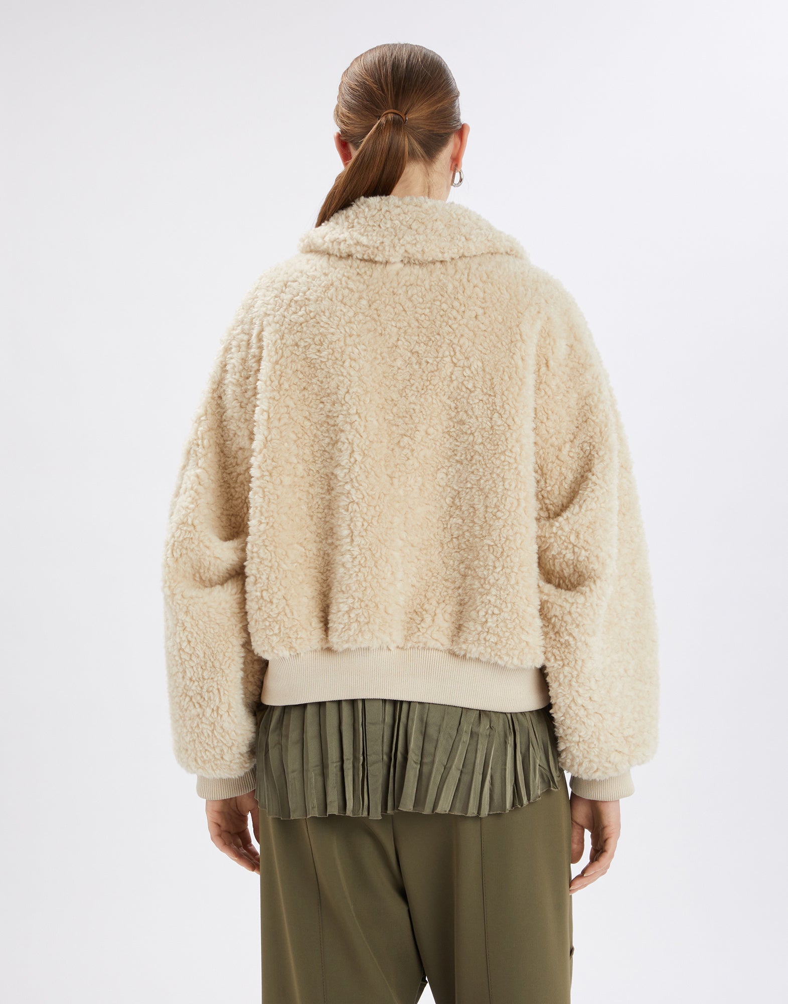 Back view of the RULER bomber jacket in cream bouclé sherpa fabric, loosely fitted with turned-down collar and wide ribbed cuffs, worn by a standing woman.