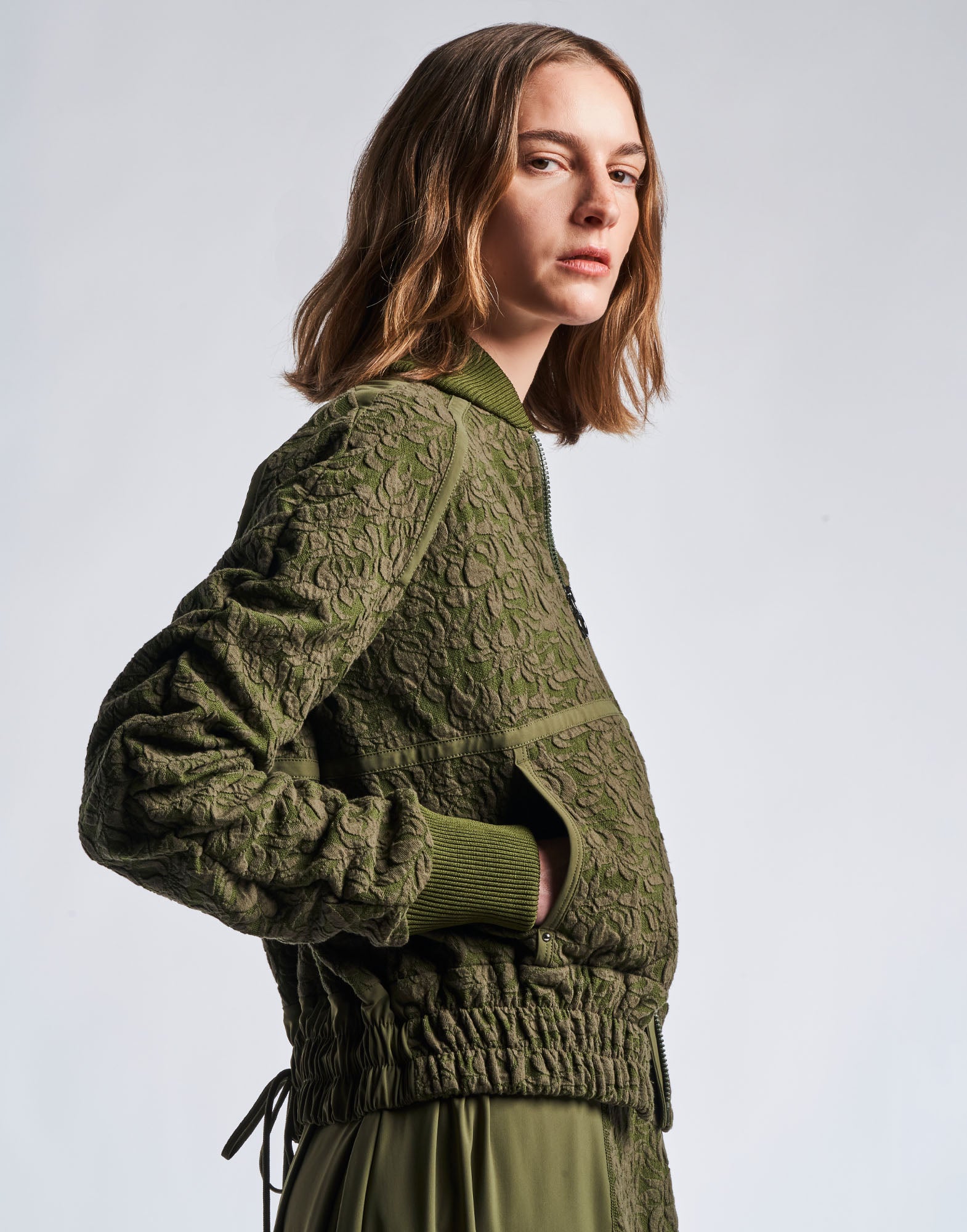 Seitenansicht einer Person, die die BOAST Bomberjacke in militärgrünem Jacquard-Baumwollmischjersey mit Baseball-Kragen, Raglanärmeln und Rippstrickbündchen trägt.