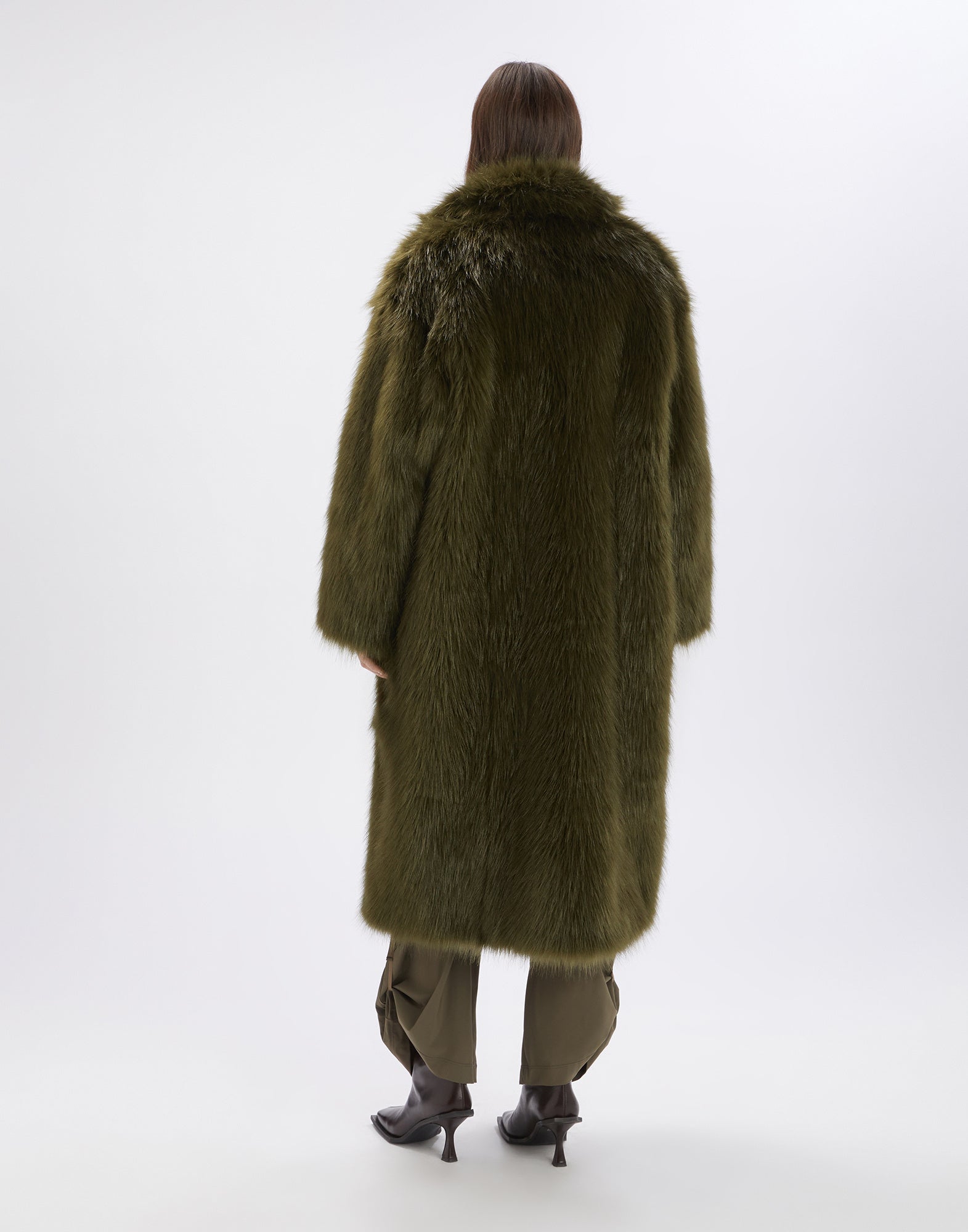 Rückansicht einer Person, die den CROSSING Kunstpelzmantel in olivgrün trägt. Der Mantel reicht fast bis zu den Knöcheln und hat voluminöses Maxi-Design.