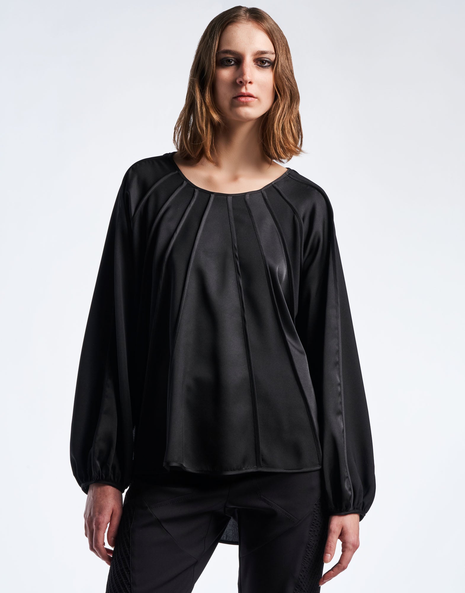 Front view of a person wearing the black GIVE CHASE top with wide round neckline, alternating matte and shiny crepe satin panels, and raglan sleeves.