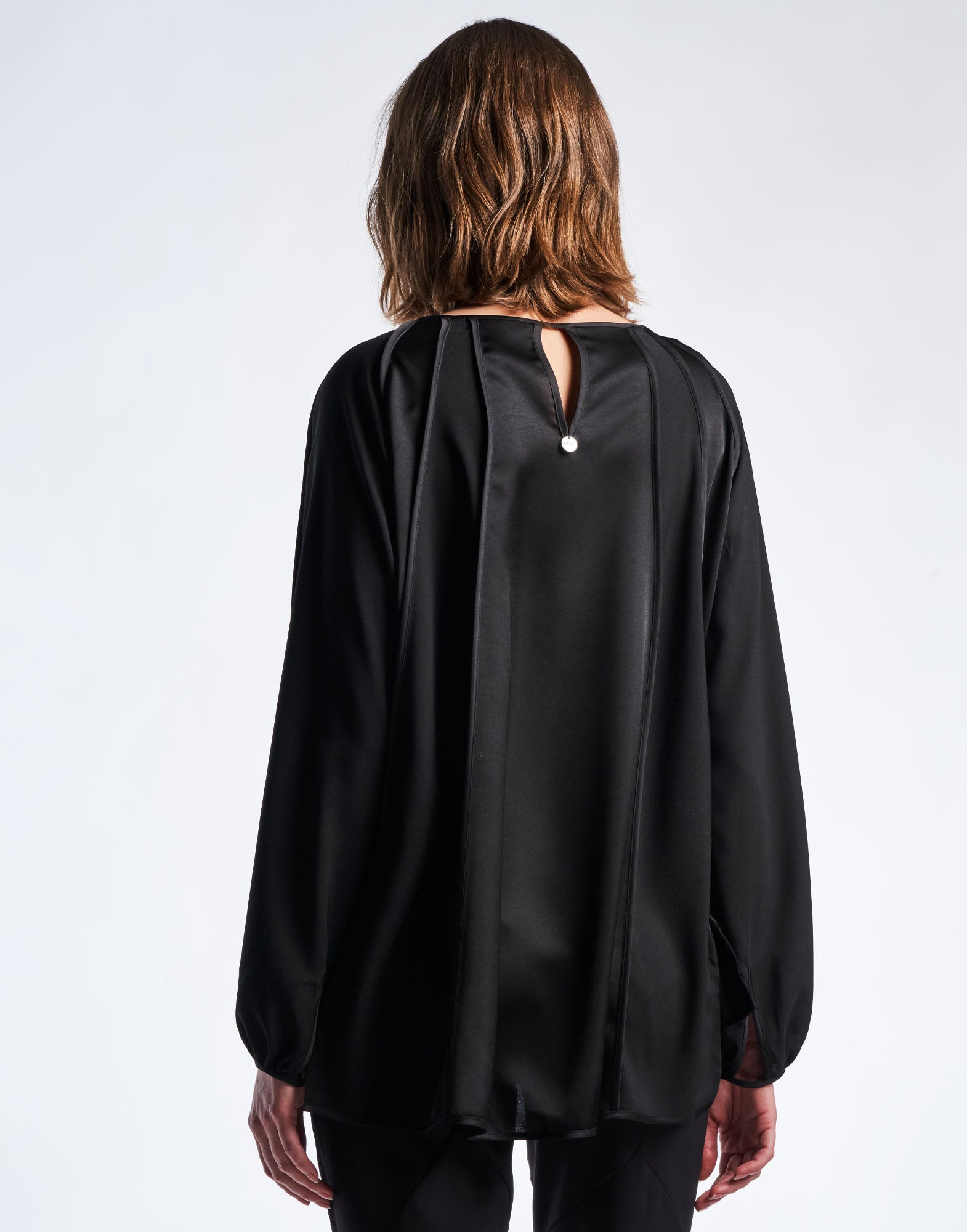 Rückansicht des GIVE CHASE Oberteils in Schwarz mit matten und glänzenden Kreppsatin-Elementen, tropfenförmiger Knopfverschluss am Nacken und lockerer, längerer Rückensaum.