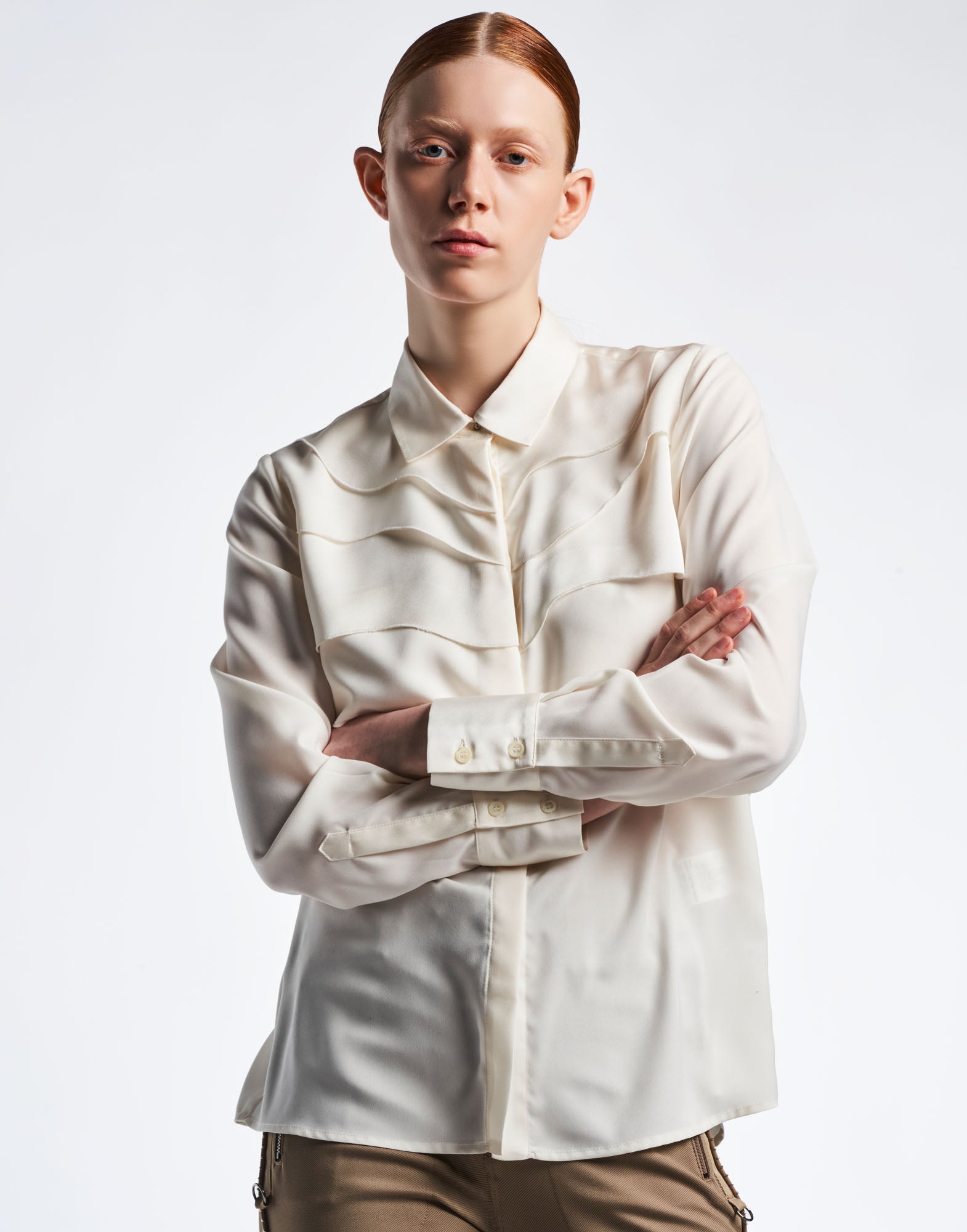 Front view: A person wears the ALTERNATE blouse with turn-down collar, concealed button placket, and curved layers on the matte and shine crepe surface.