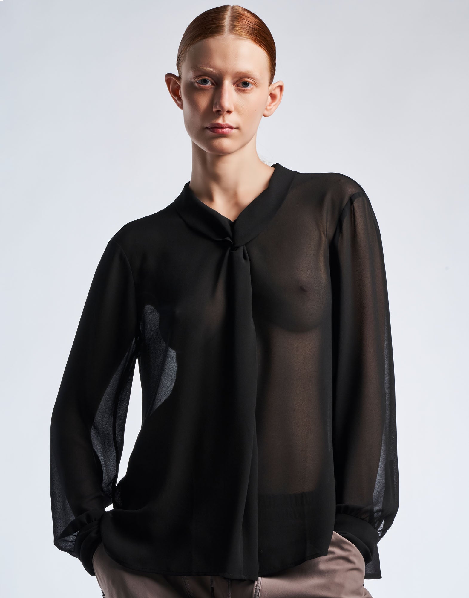 Frontalansicht: Modell trägt die VICE VERSA Bluse in transparentem schwarzem Funktions-Georgette mit weichem Klappkragen, Wickelkonstruktion und langen Ärmeln.