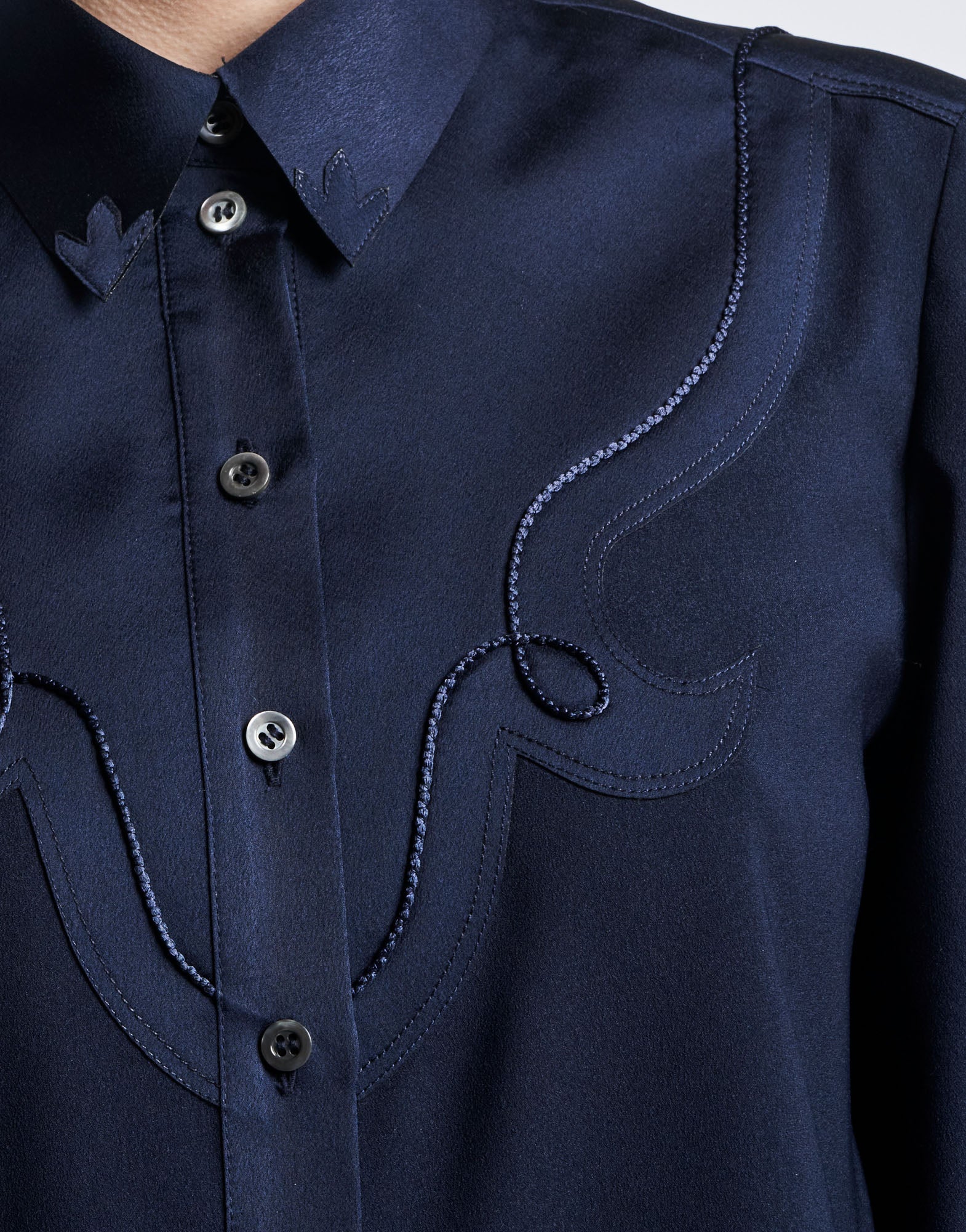 Detail view: APPRECIATION displays the front of a Western-style blouse made of technical satin-back crepe with alternating shiny and matte panels, mother-of-pearl buttons, and decorative cord work over the chest and shoulders.