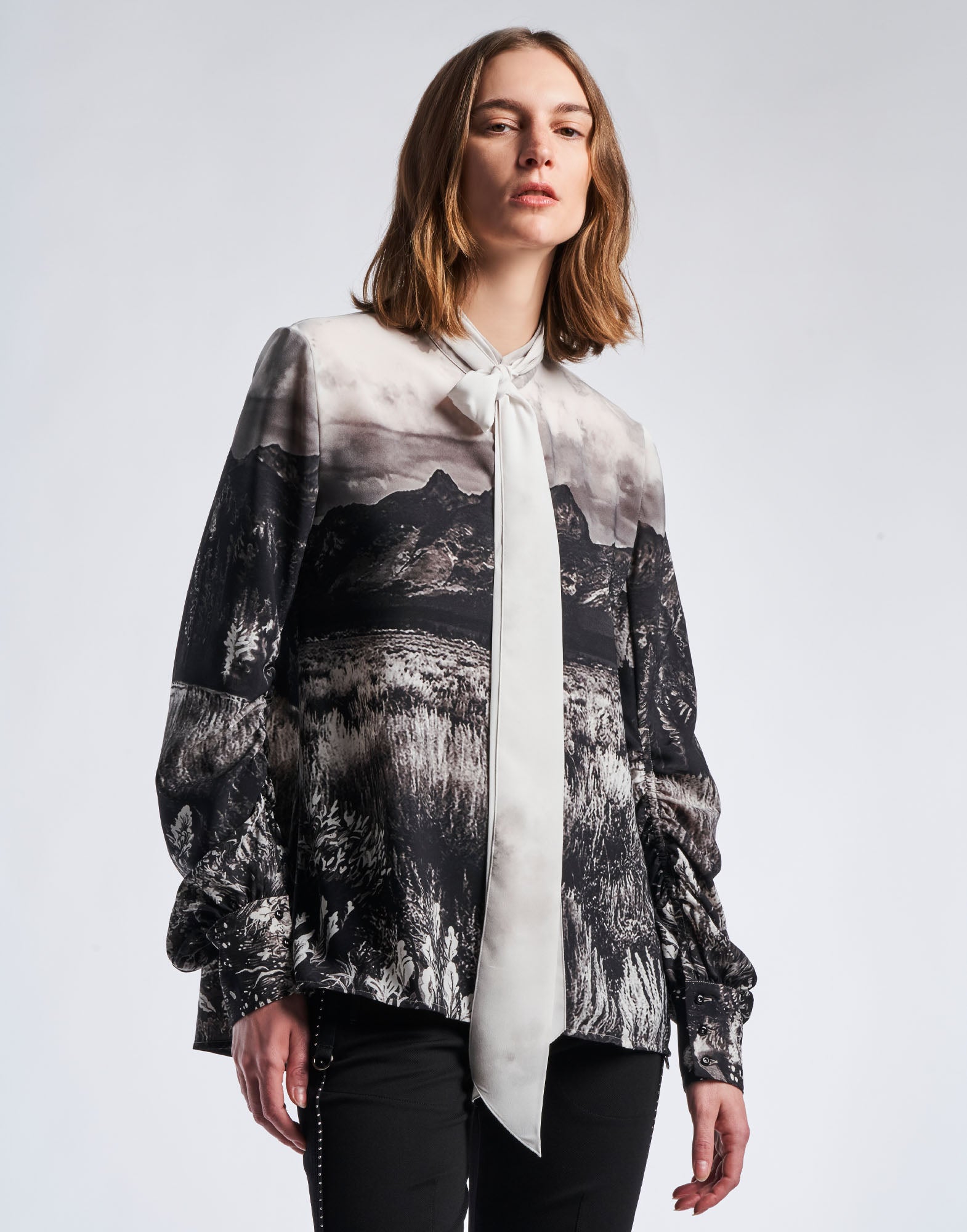 Front view: person wears the AMAZEMENT blouse in black and white 'Wyoming' printed crepe, stand collar with tie and ruched sleeves.