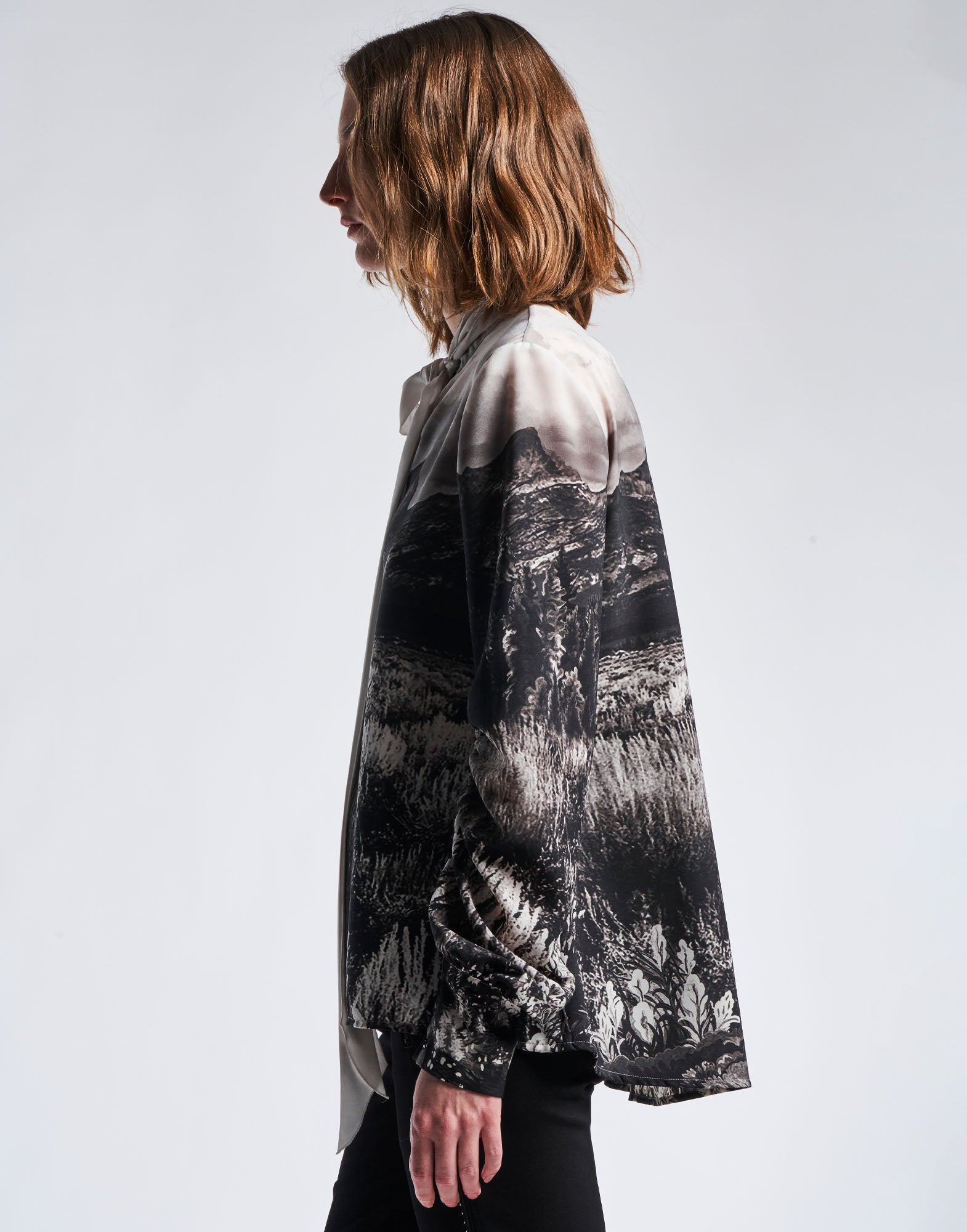 Side view of a person wearing the AMAZEMENT blouse in black and white functional crepe with Wyoming print. Visible are the stand collar, the ruched sleeves, and the wide rounded hem.