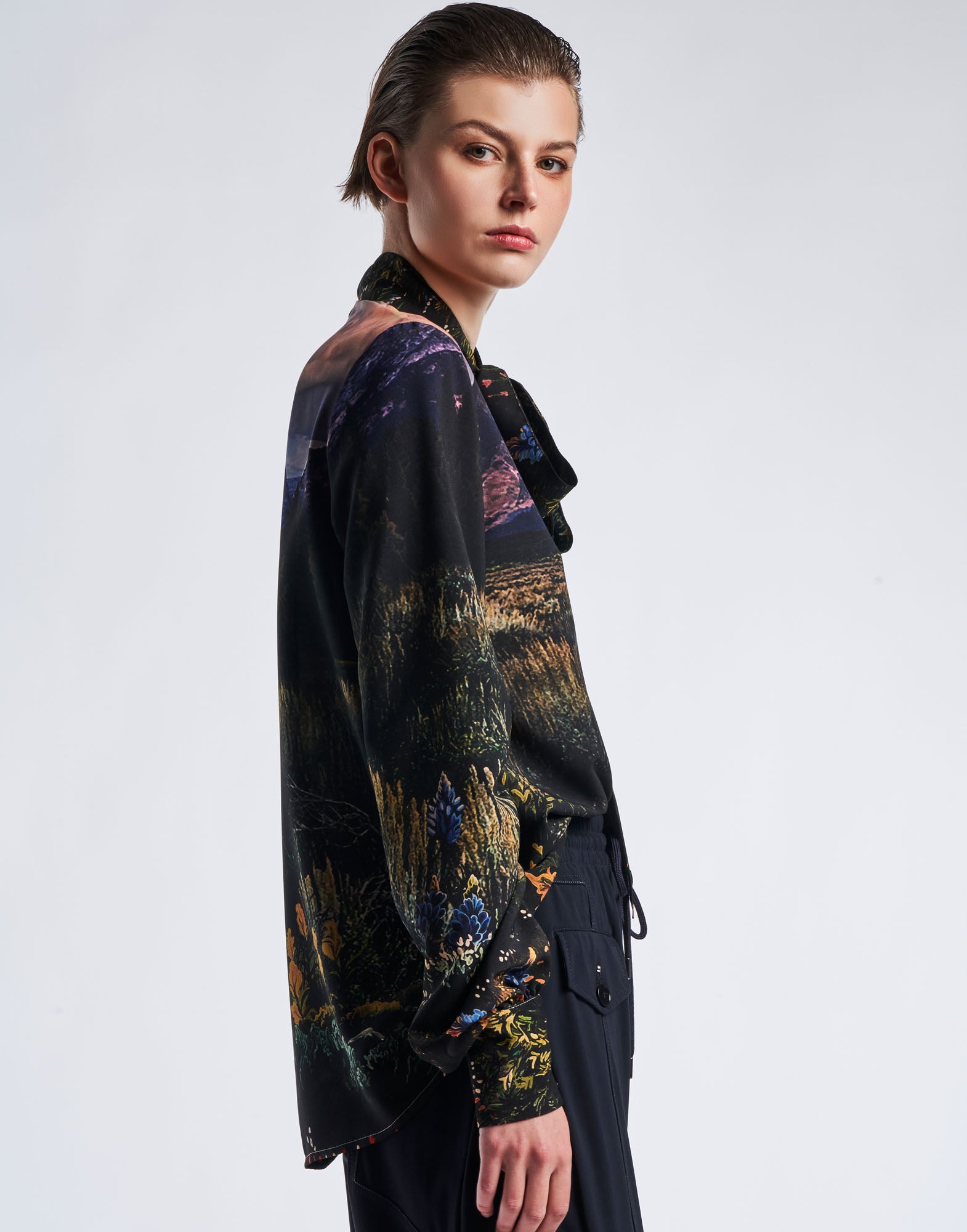 Side view of a person wearing the AMAZEMENT blouse in functional crepe with multicolour 'Wyoming' print. Visible: stand collar, tie band, and ruched sleeves.