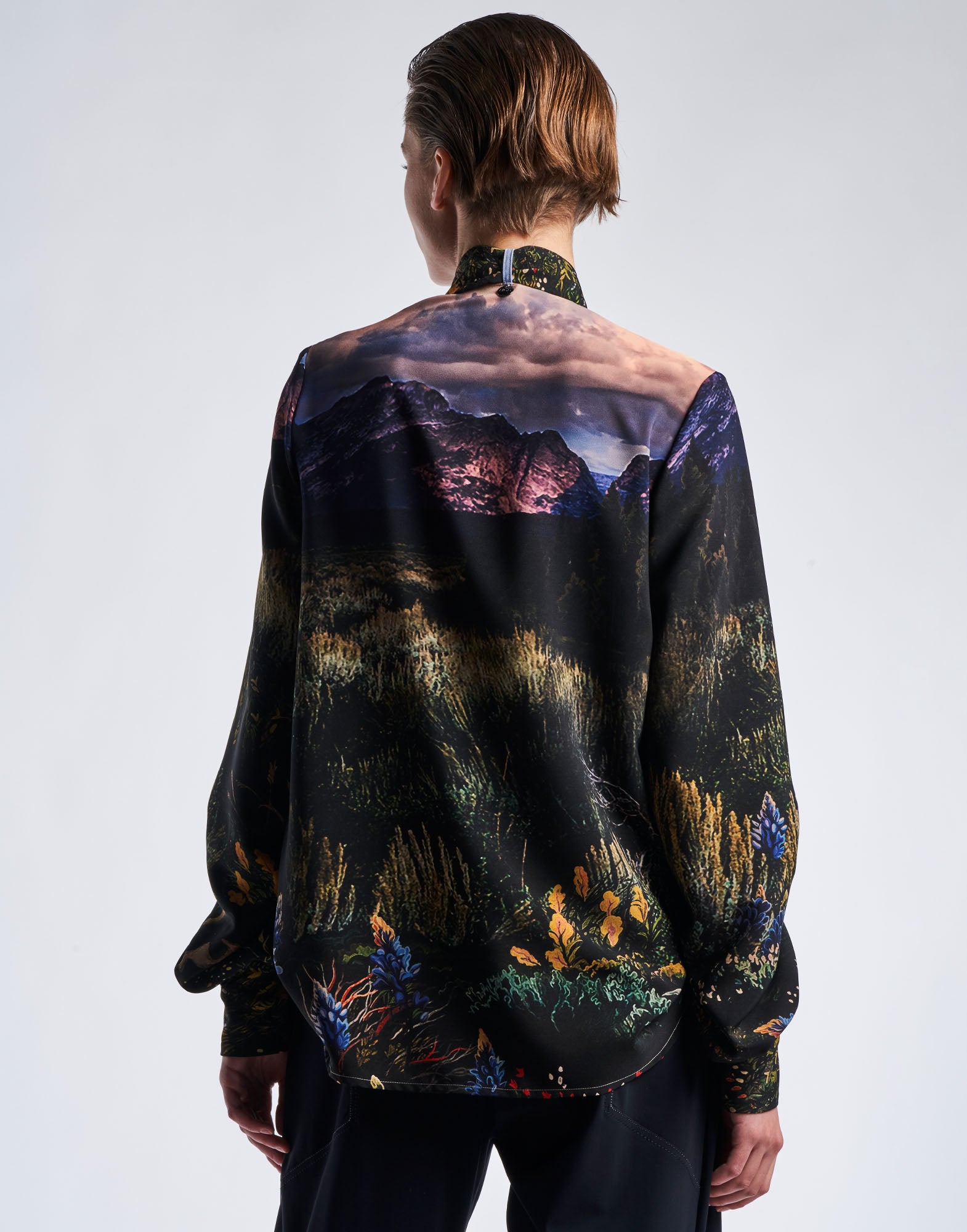 Rear view of a person wearing the AMAZEMENT blouse; blouse made from functional crepe with multicolour 'Wyoming' print, stand collar, and wide curved hem.