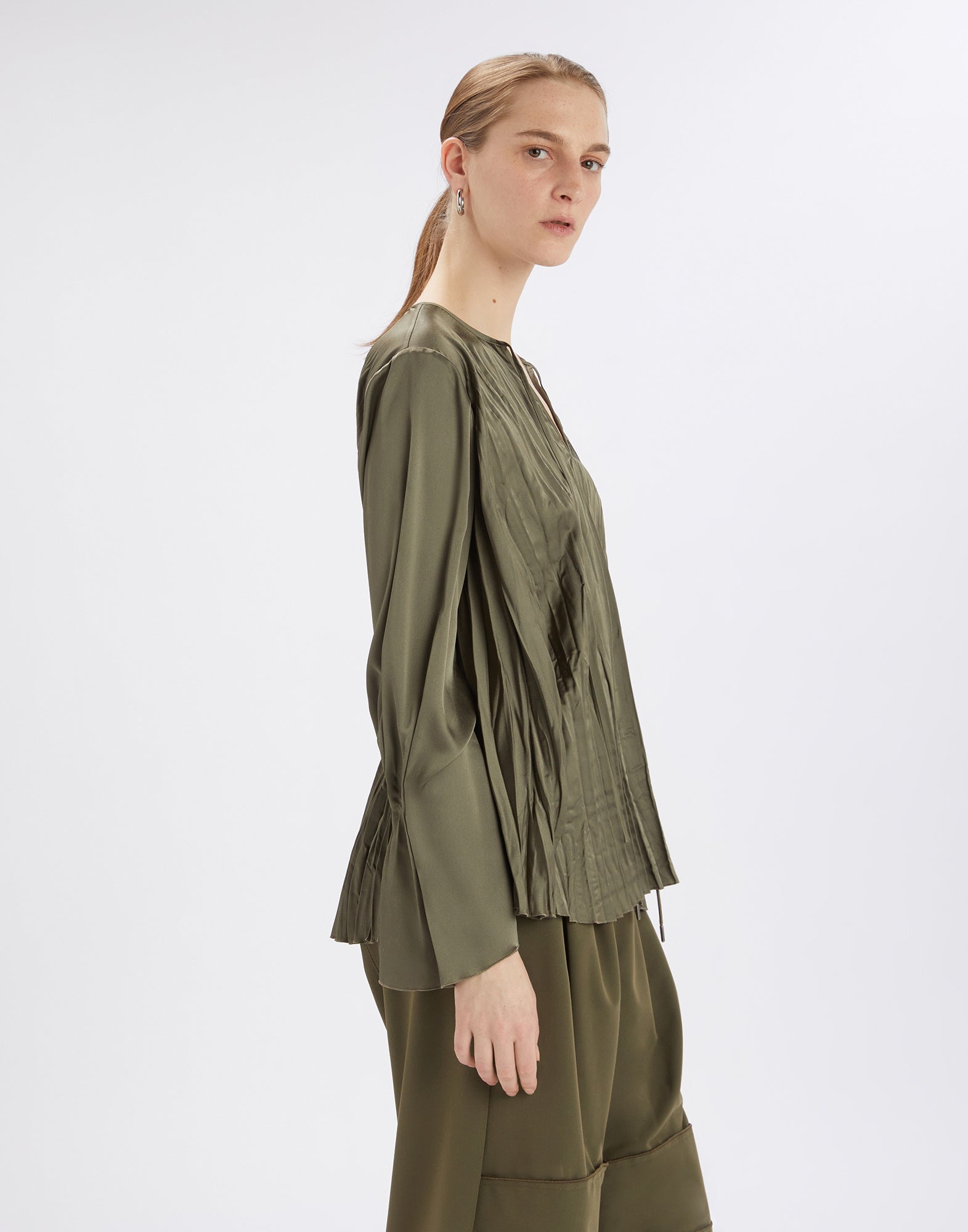 Seitenansicht der Bluse ONTOP in Olivgrün, getragen von einem Model. Die Bluse aus glänzendem Satin zeigt einen leichten Plisseeeffekt und weite Ärmel.