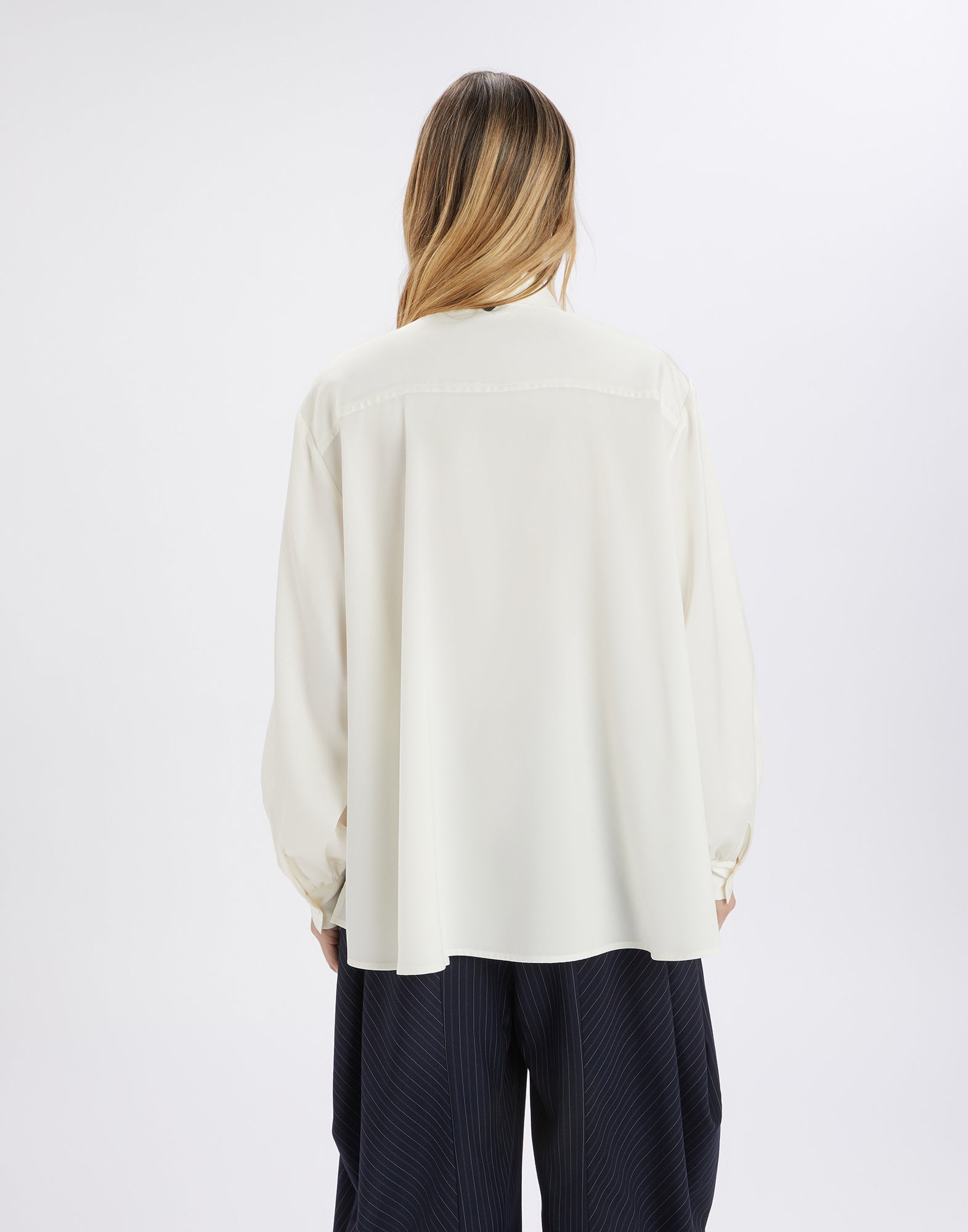 Back view of the MERYL blouse, loosely draped with long sleeves, turned-down collar and slightly sheer georgette, worn by a woman.