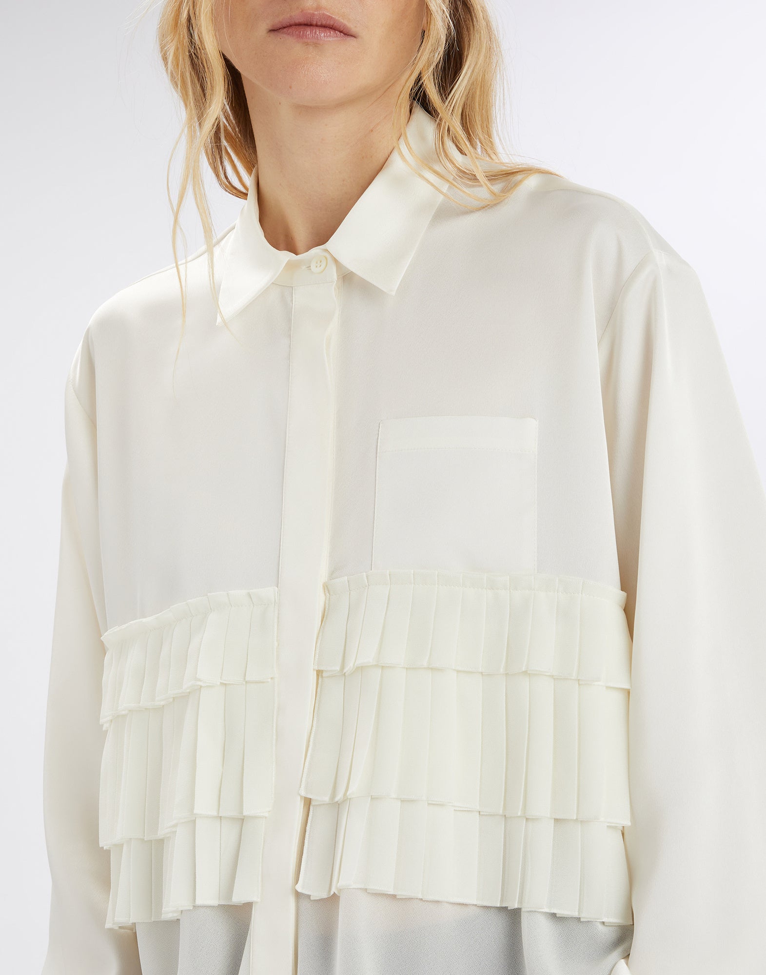 Front view of the MERYL blouse, worn by a person, featuring cream satin, turn-down collar, concealed button closure, and three pleated georgette ruffles on the upper body.