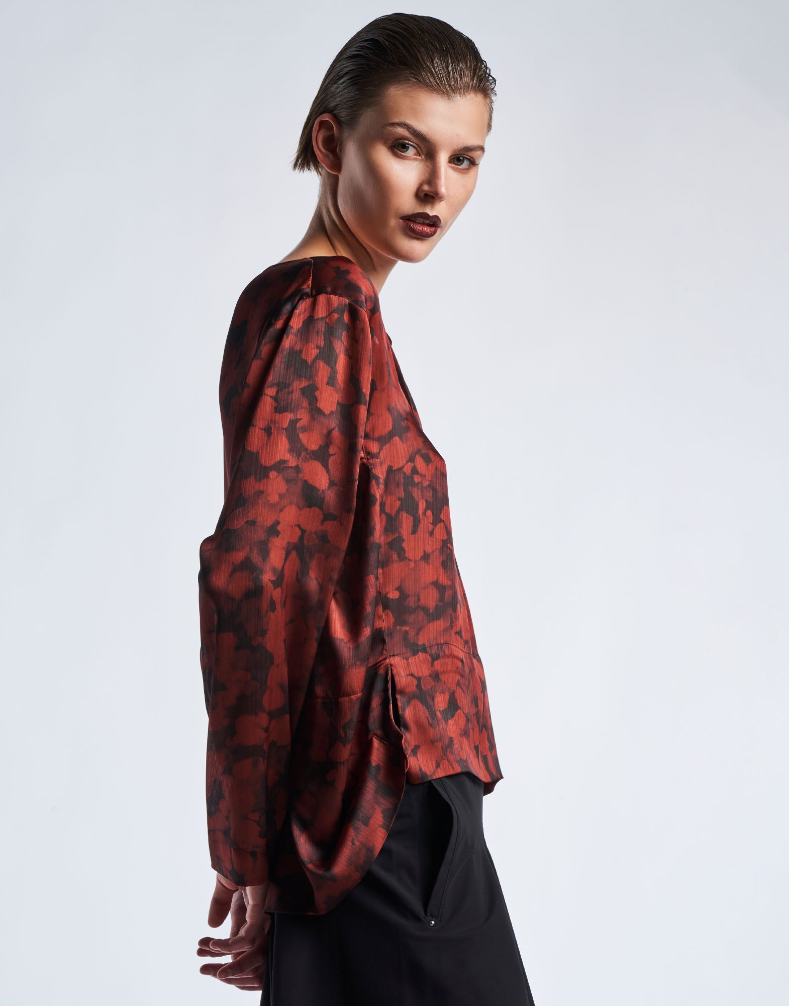 Side view of the ALONE top in technical crepon with black and claret red geo animalier digital print, oversized shoulders, and knot detail at the front.