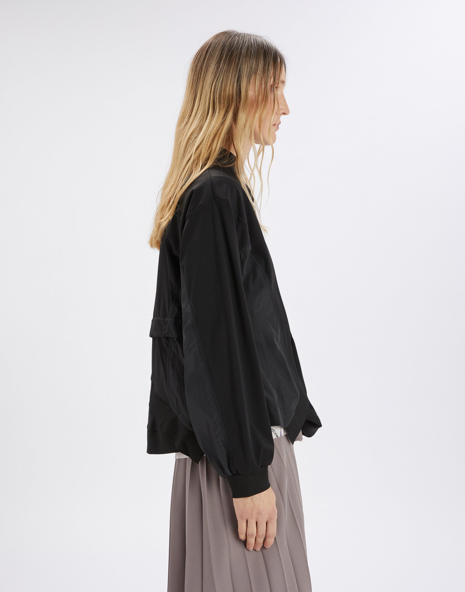 Side view: model wears black SLINK sweatshirt with sculptural silhouette, stand collar, long sleeves, ribbed cuffs, and asymmetric hem.