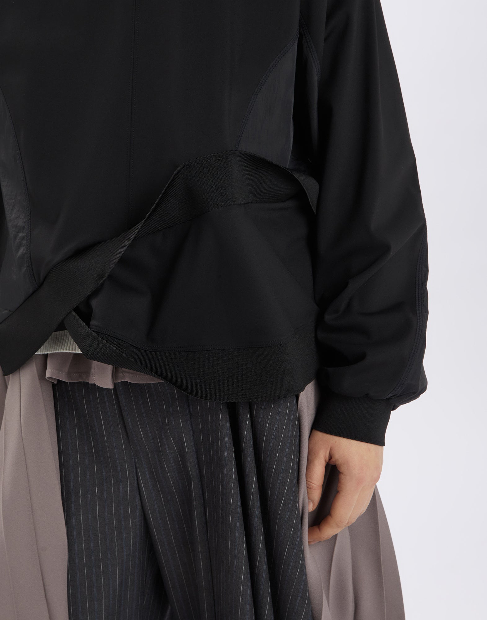 Detail view of SLINK, black neoprene sweatshirt with nylon inserts at hips and underarms, asymmetric hem and ribbed cuffs visible.