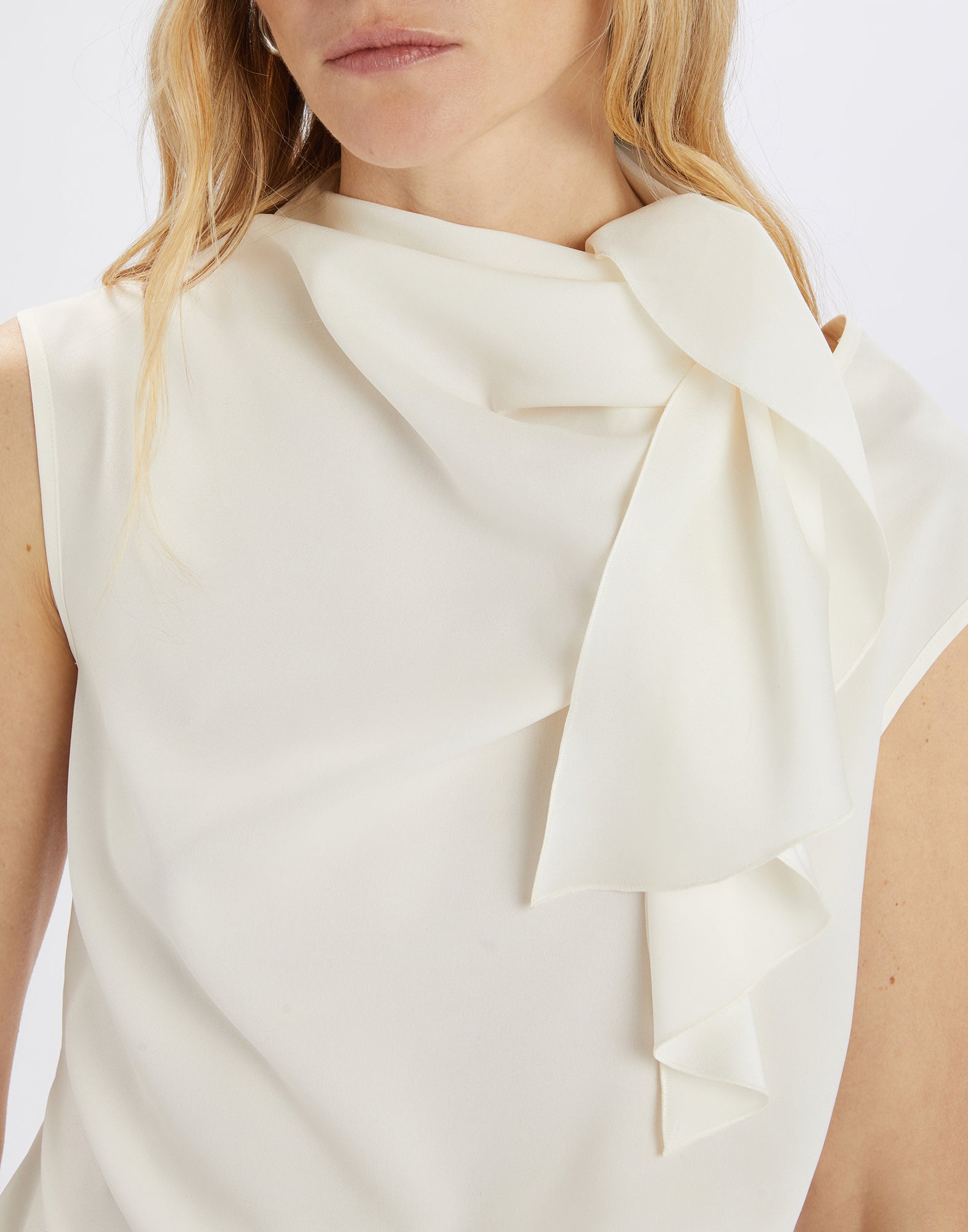 Front detail view: WALTON sleeveless top in flowing cream satin with side jabot collar and asymmetric hem, loosely tied around the neck.