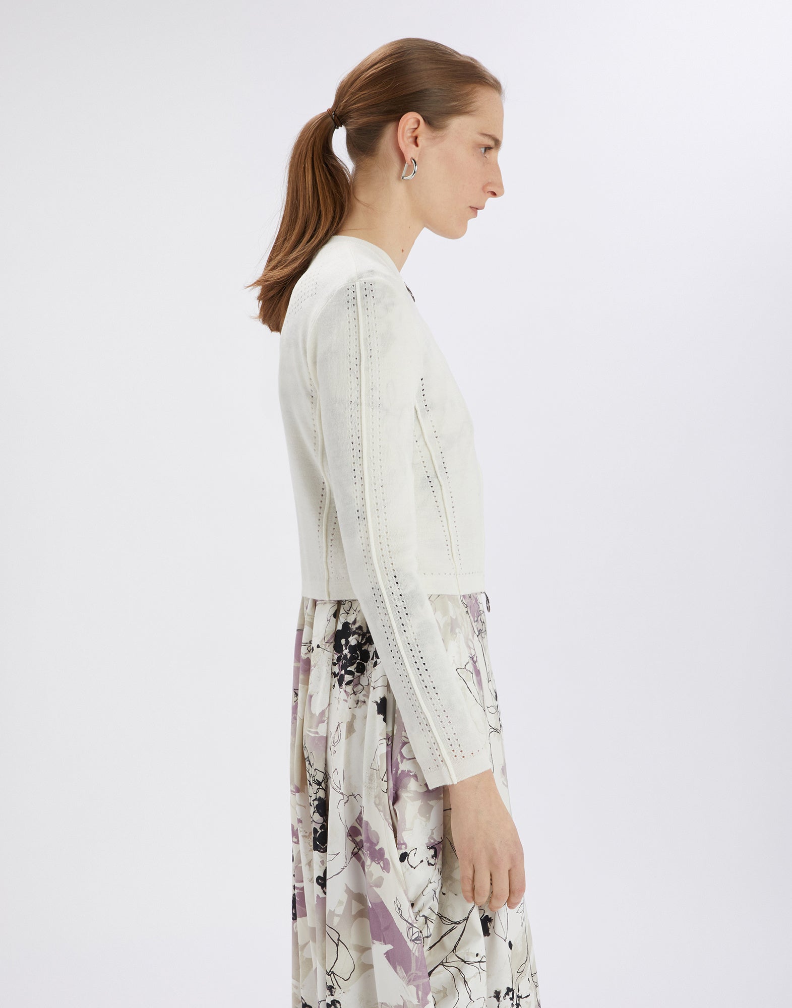 Side view of a woman wearing the SKITTER cardigan; slim-fit, cropped knit with openwork pattern, crewneck and ribbed cuffs.