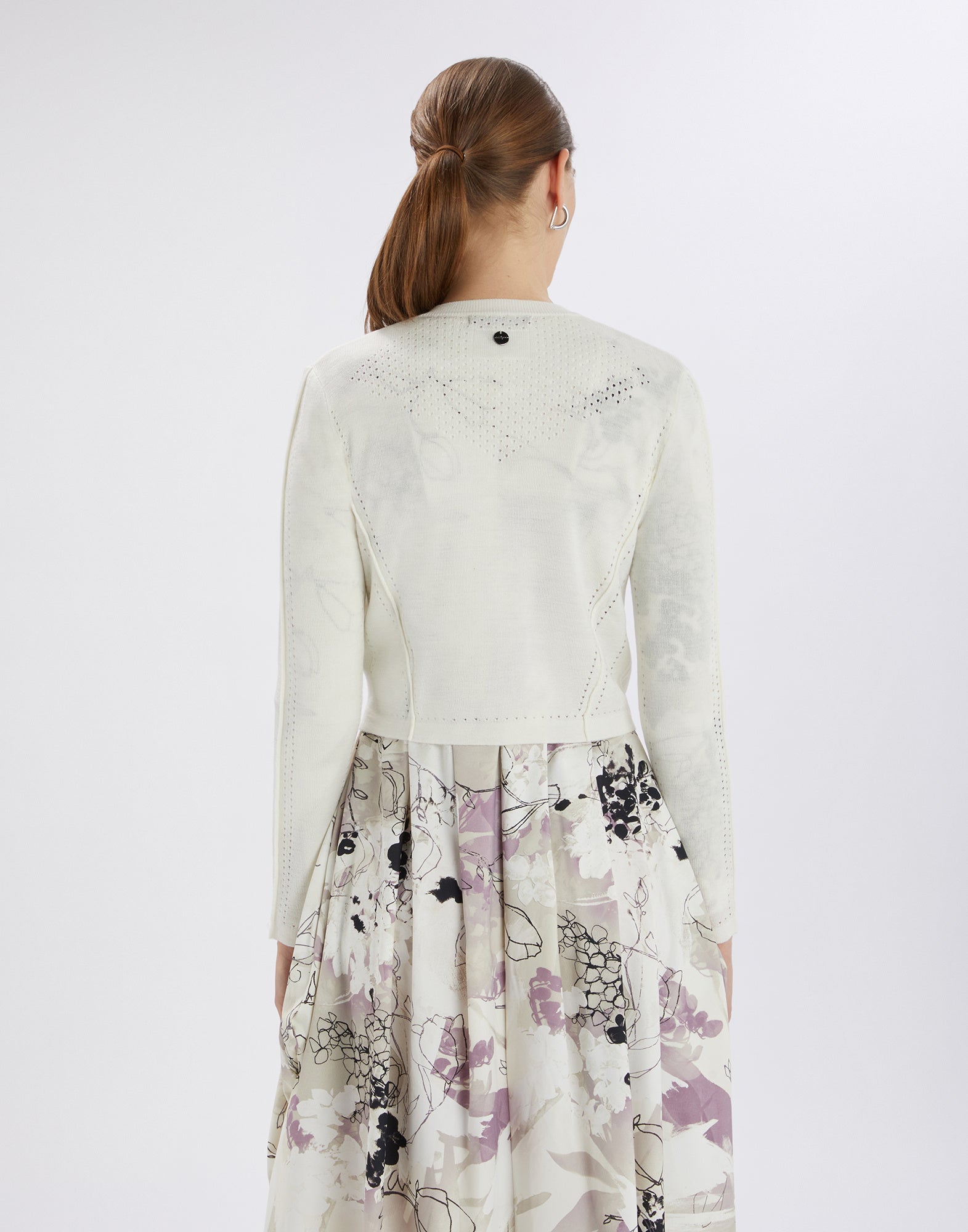 Back view of a woman wearing the white SKITTER cardigan; accentuates the waist through openwork pattern and shows a special net effect on the back.