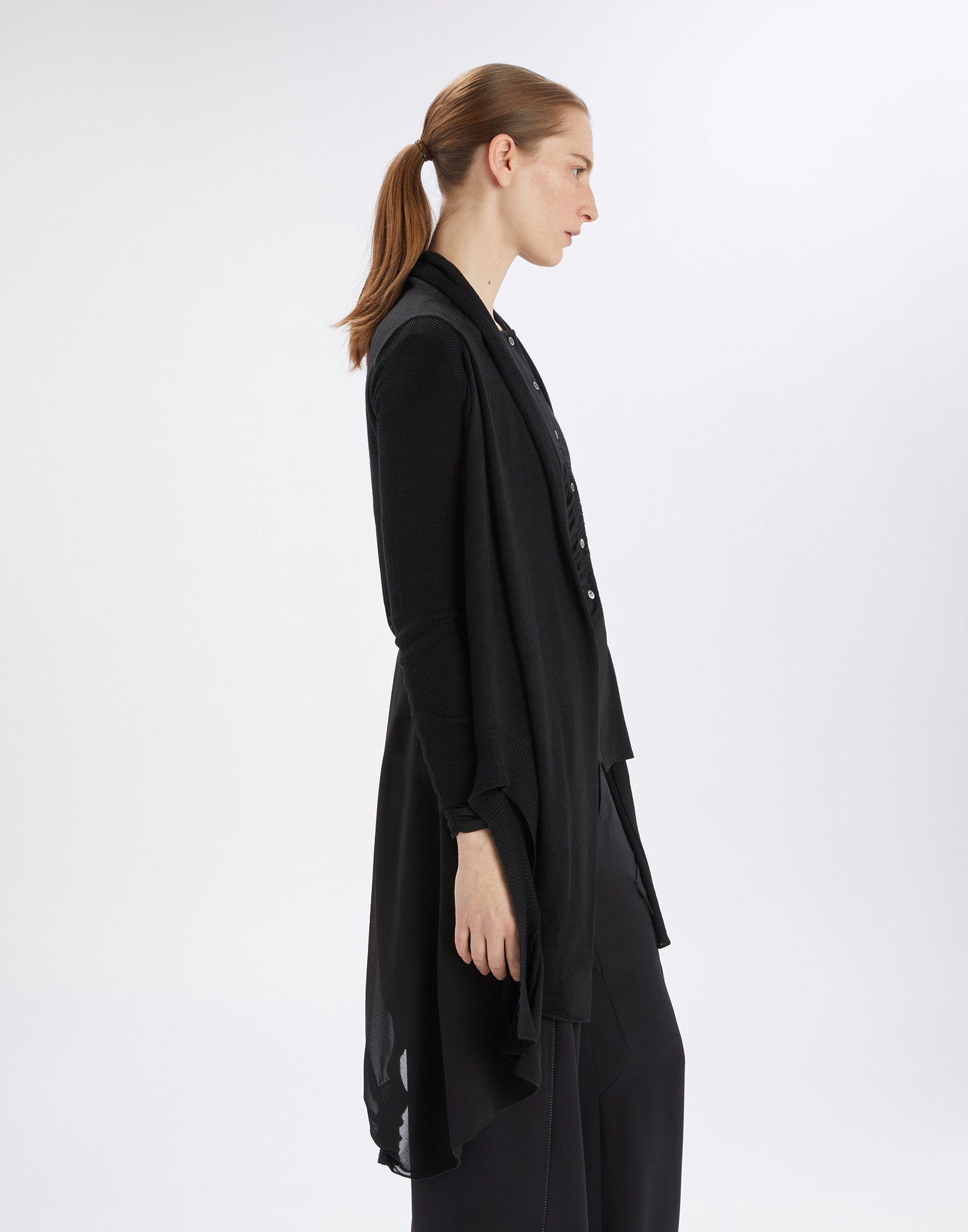 Seitenansicht einer Person, die einen schwarzen Cardigan namens SLIVER trägt. Der Cardigan ist weit geschnitten, mit Raffungen am Rücken und unregelmäßigem Saum.