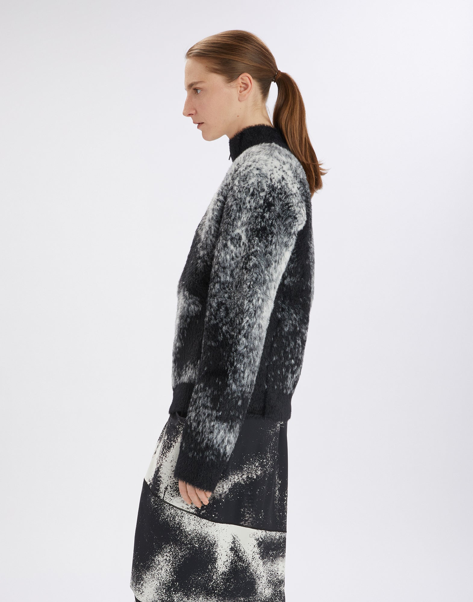 Seitenansicht eines Models, das den SUMMON UP Cardigan in bicolor Jacquard mit weichem, fluffigem Finish und floralem Muster am rechten Ärmel trägt.