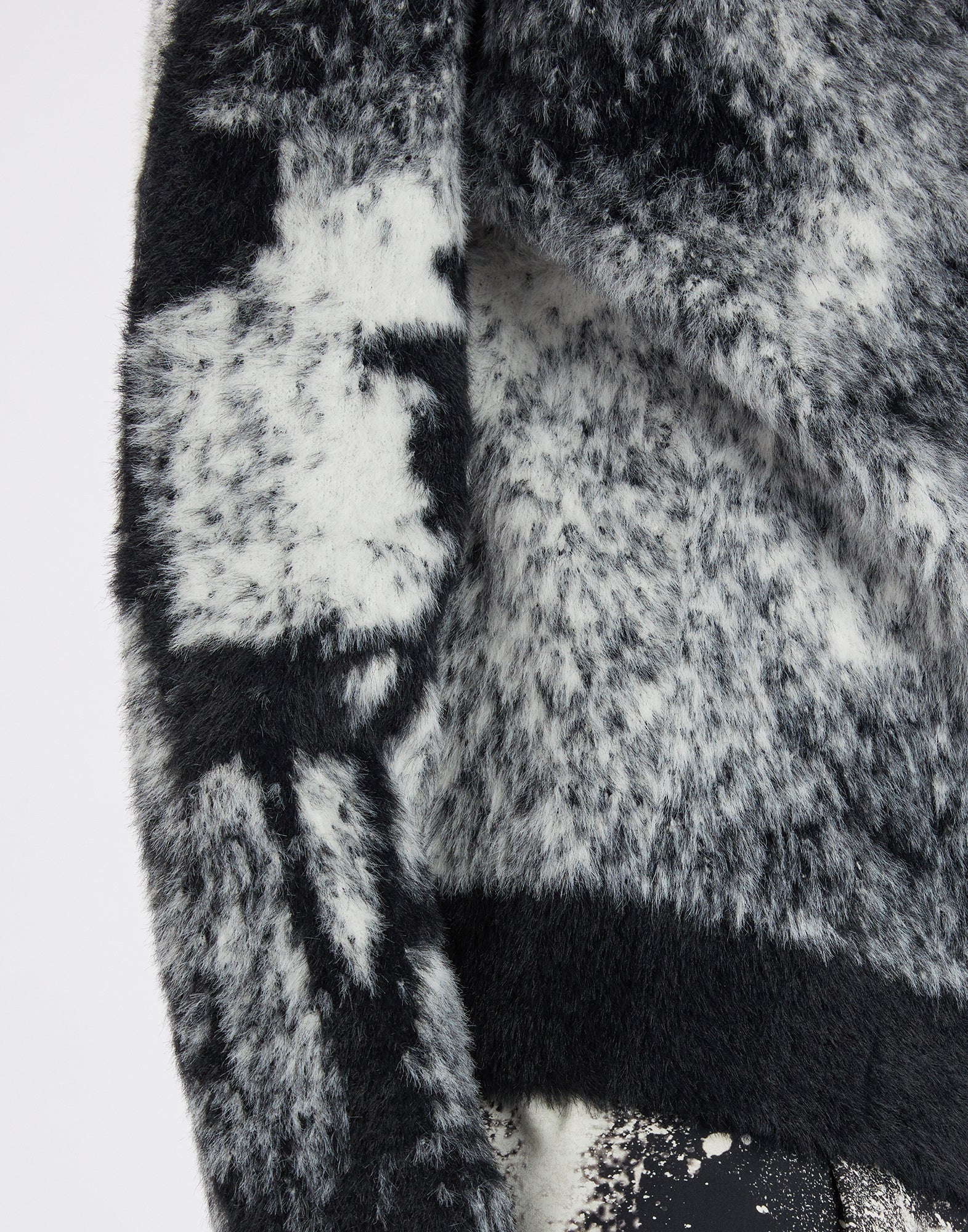 Detailansicht des SUMMON UP Cardigans aus weichem, flauschigem bicolor Jacquard. Florales Muster am rechten Ärmel, sichtbare weiche Textur in Schwarz und Weiß.