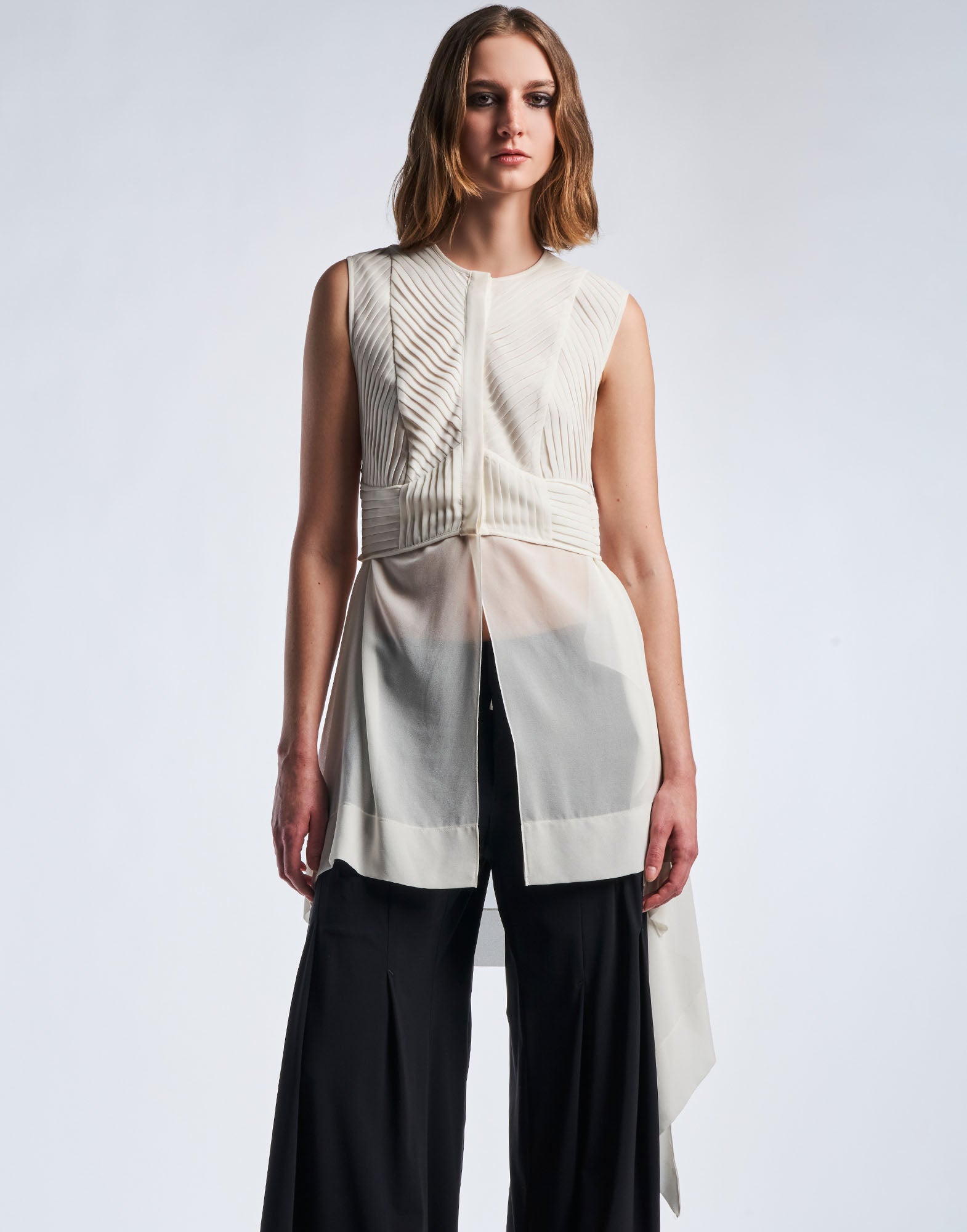 Front view: PLAYFUL displays a sleeveless tunic in semi-sheer cream technical georgette with a structured, diagonally ribbed bodice and handkerchief hem.