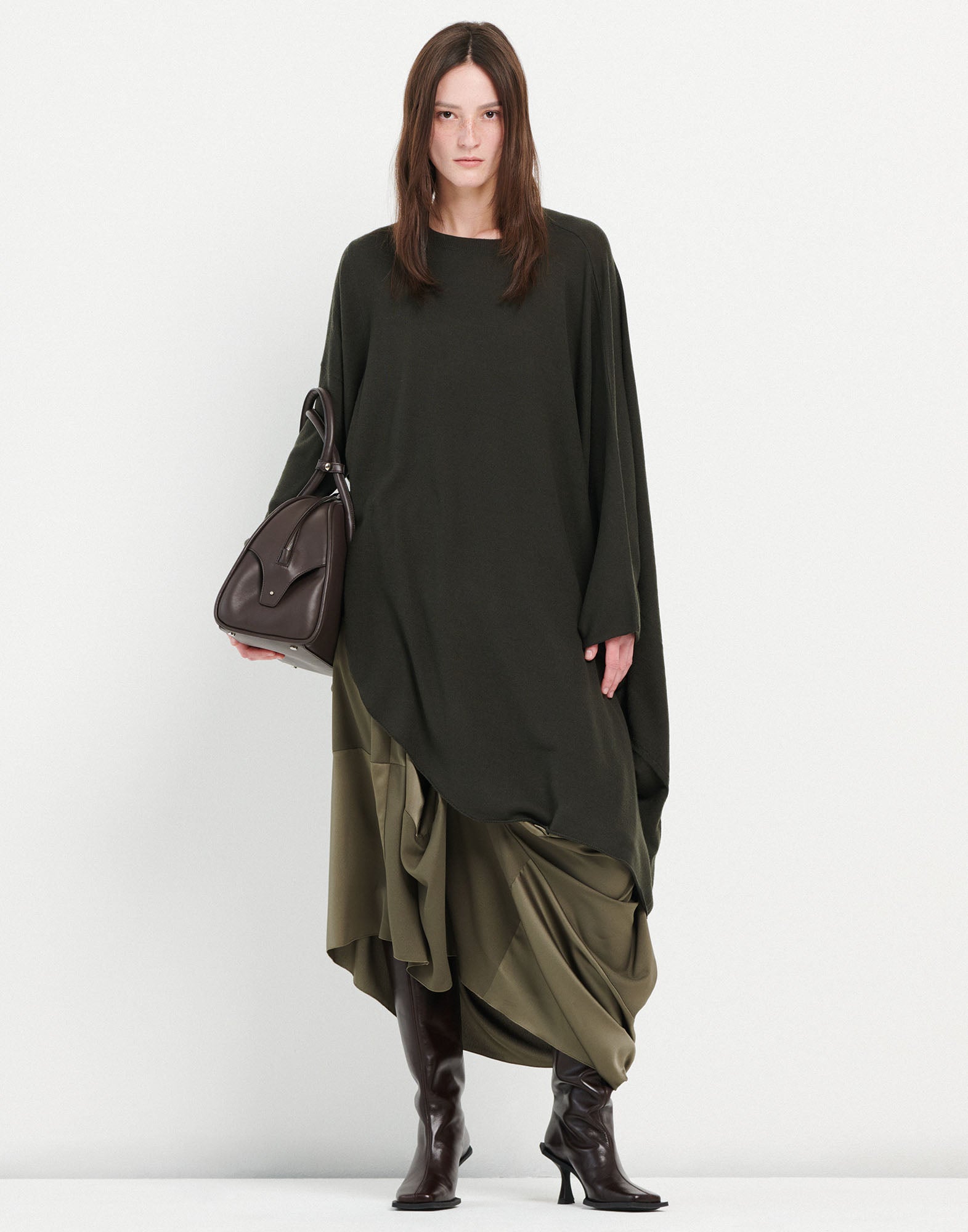 Front view of the ON SET tunic with asymmetric hem, draping loosely over an olive dress, worn with long sleeves and brown boots.