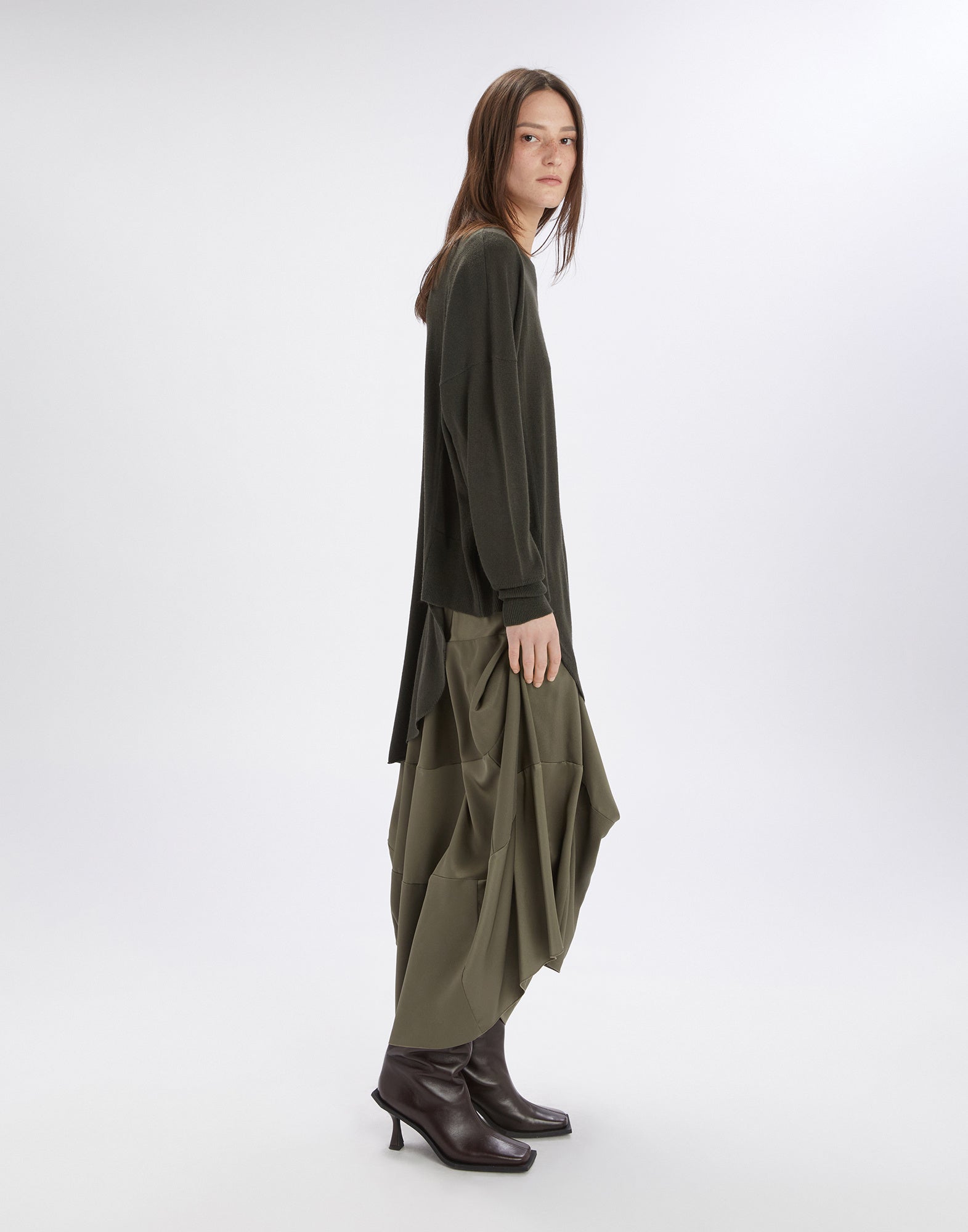 Side view of a woman wearing the ON SET tunic with asymmetric cut. The lightweight wool blend piece drapes diagonally from the right hip to below the left knee.