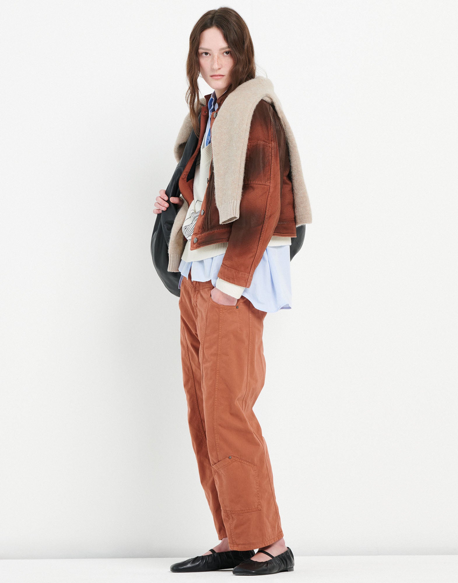 Side view of a person wearing FURORE trousers; brown-orange bootcut trousers with patch pockets and visible seams, paired with a brown jacket.