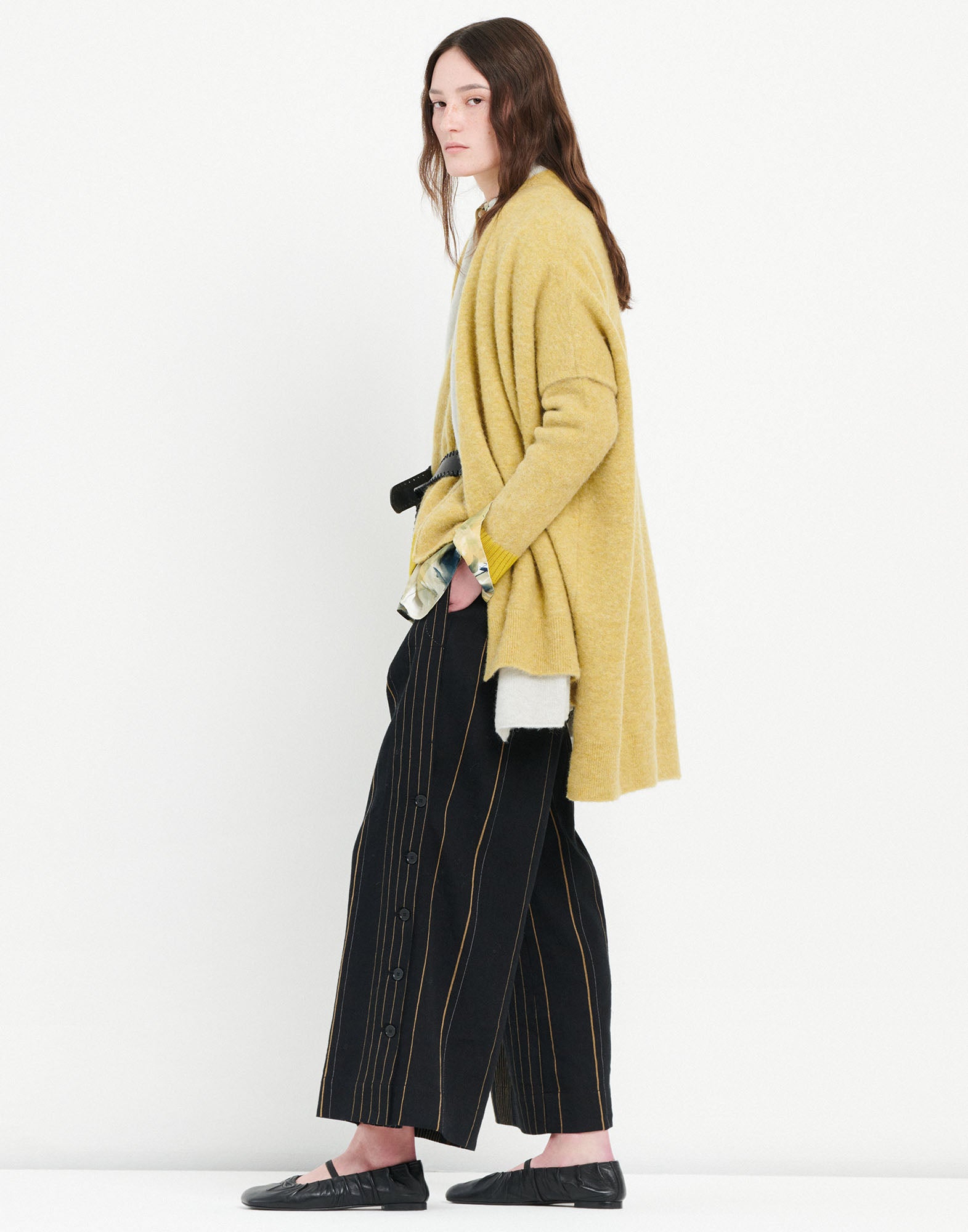 Side view of a person wearing SWALLOW trousers; the black trousers feature vertical colorful stripes, side button placket, and ankle length.