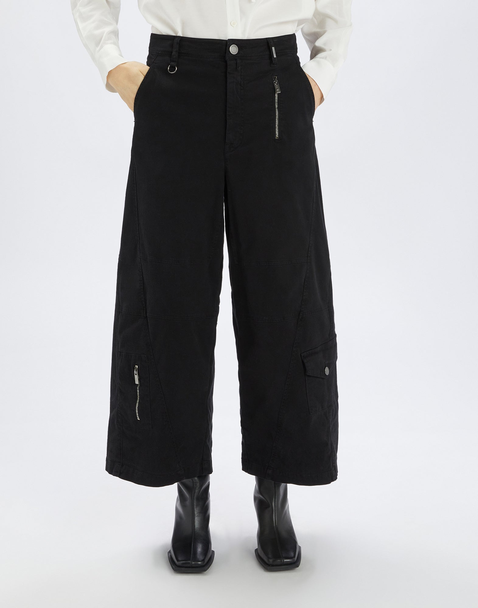 Front view of OUT RUN trousers, black, wide silhouette from hip, asymmetric seams, applied pockets, metal zippers, and visible topstitching.