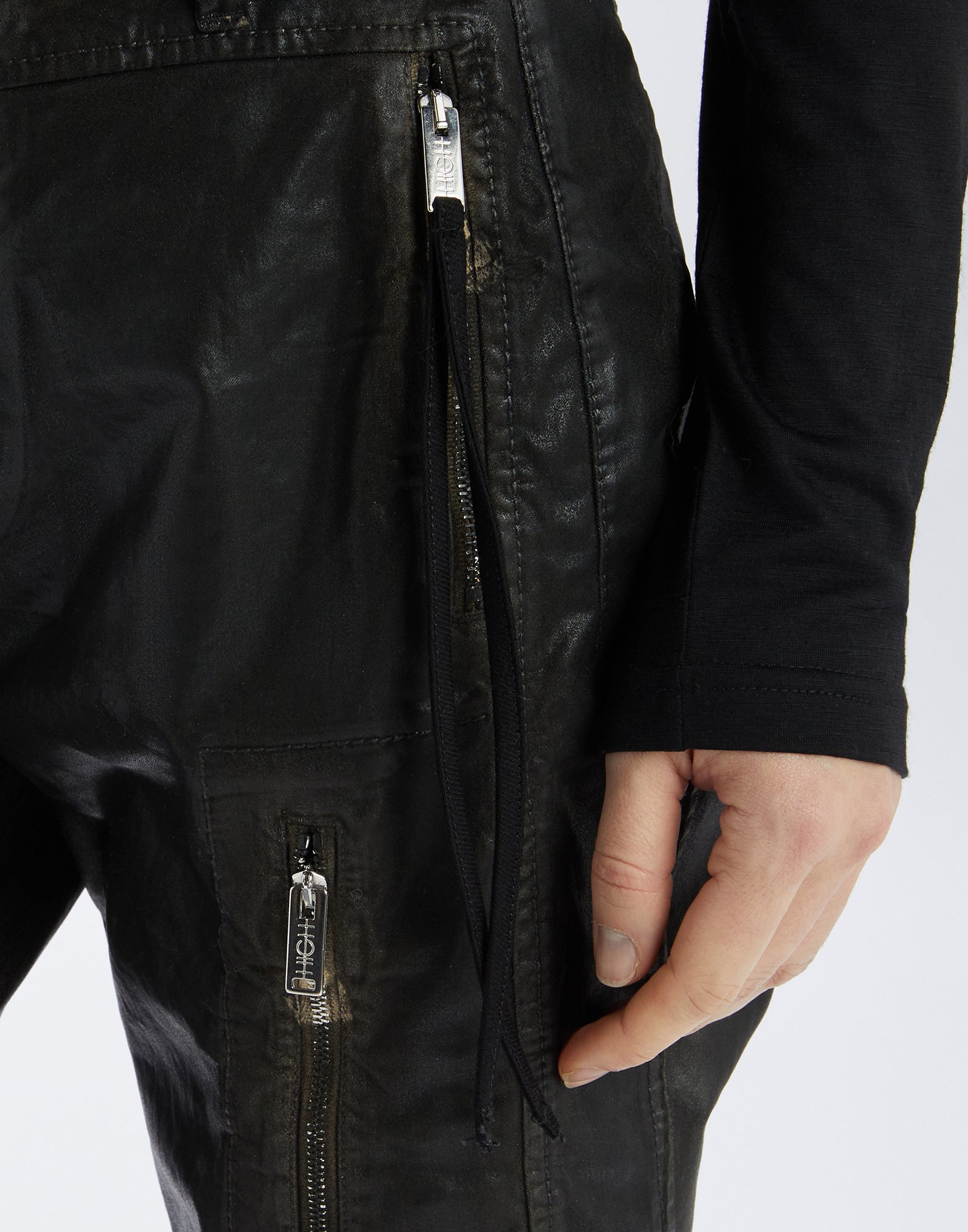 Close-up view of INKLING jeans shows leather-like finish, silver zippers on front and side pockets, visible topstitching and waistband loop.